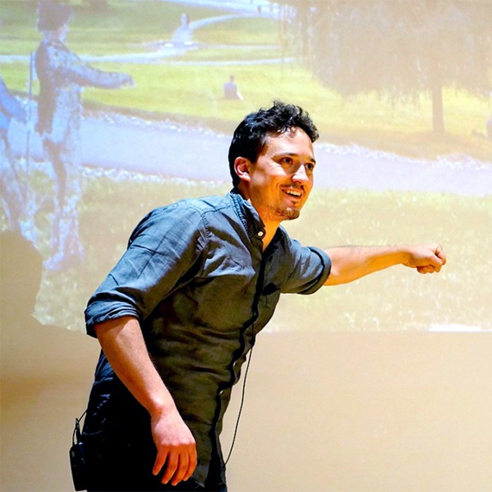 Man gesturing toward a projected outdoor scene during a presentation