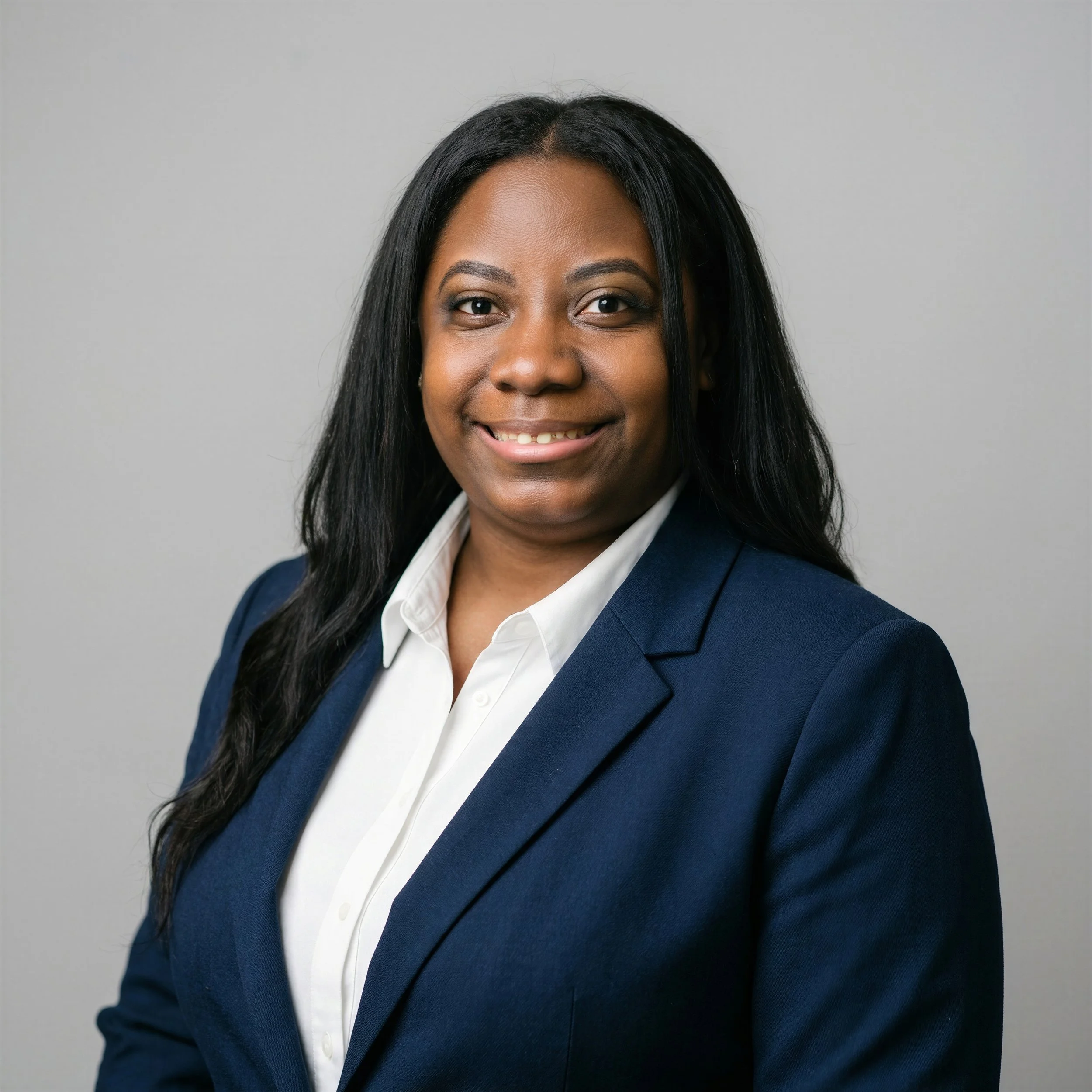 Close-up of an African American woman with long black hair, smiling, wearing a navy blazer and white shirt against a gray background.