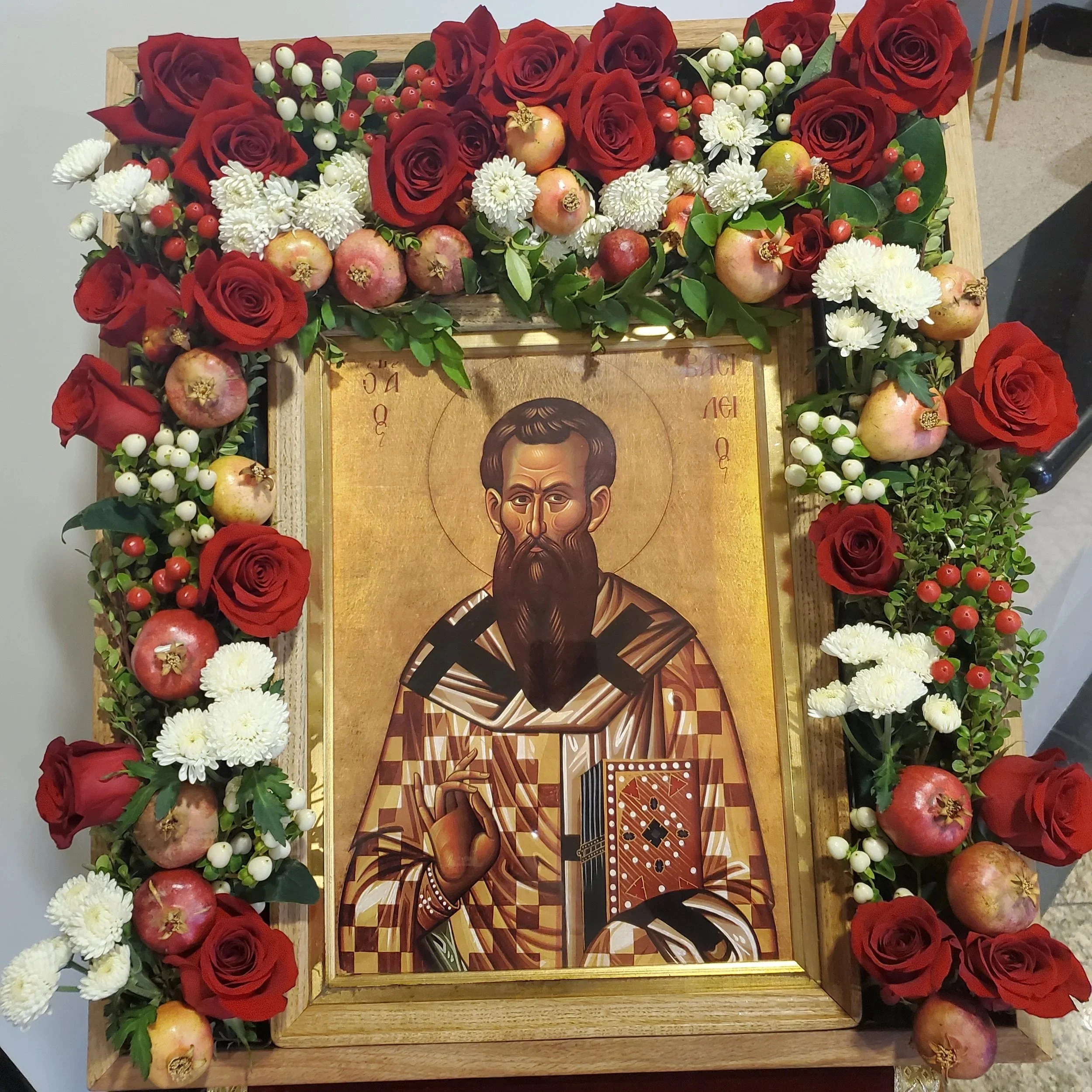 Icon of a bishop saint framed with red roses and pomegranates