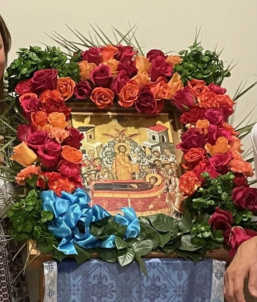 Feast icon framed with red and orange roses and a blue ribbon