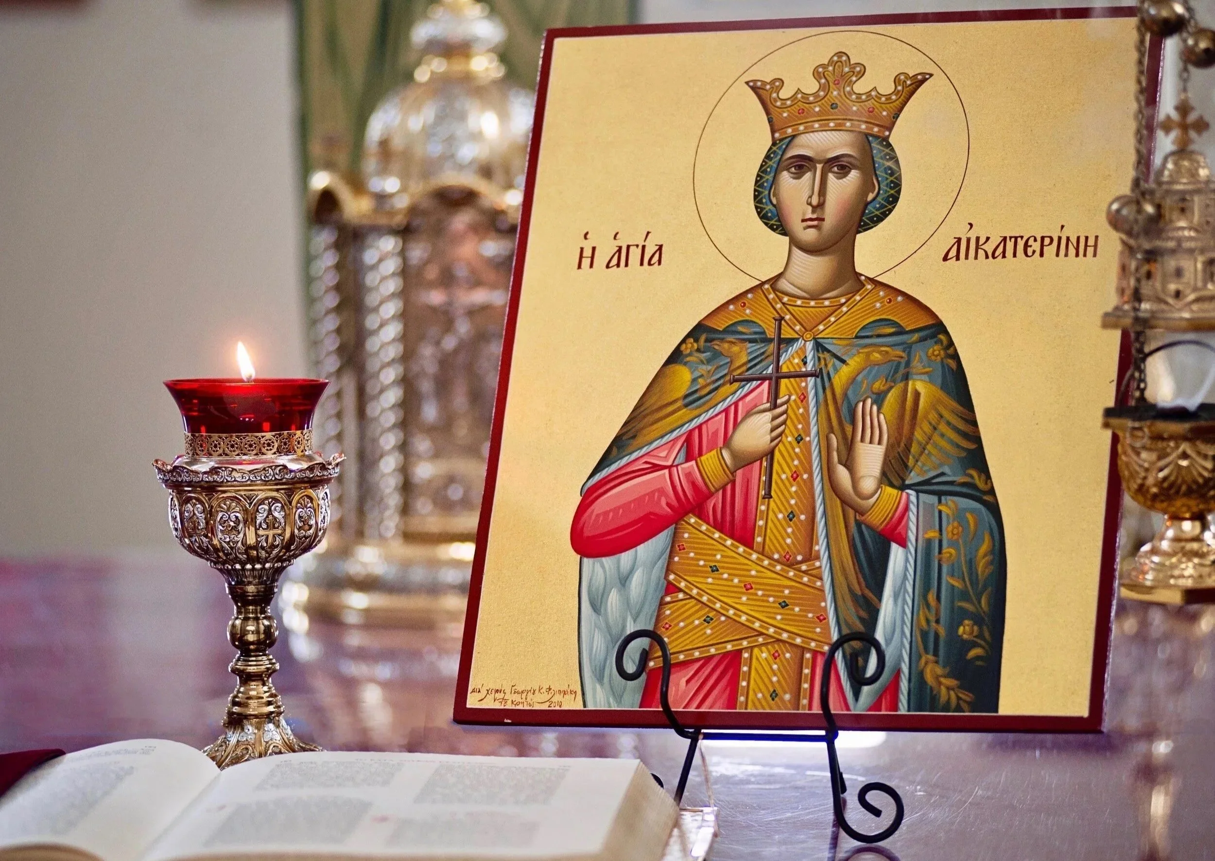 Icon of Saint Katherine on a stand beside a red vigil candle and an open book