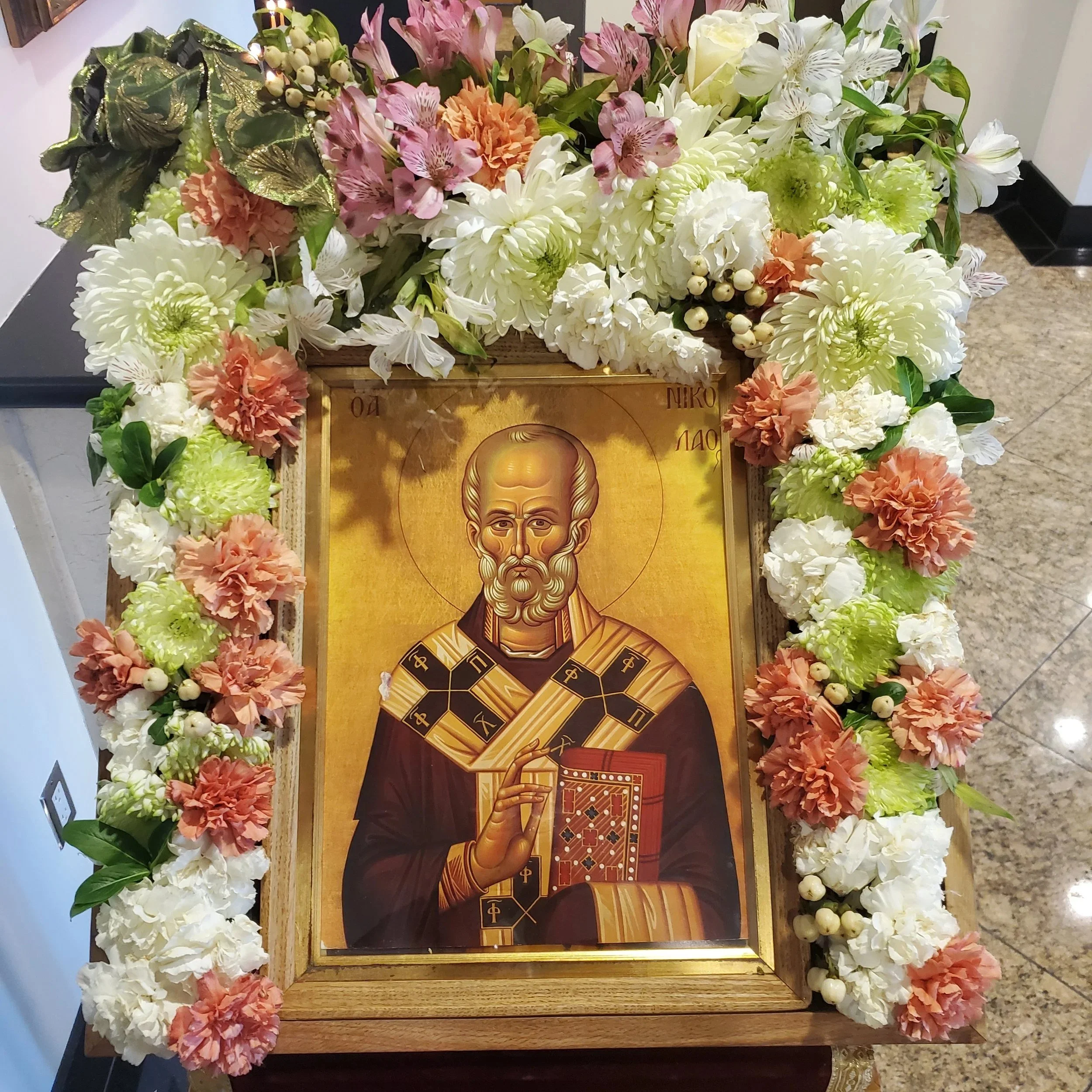 Icon of a bishop saint framed with pink and white flowers