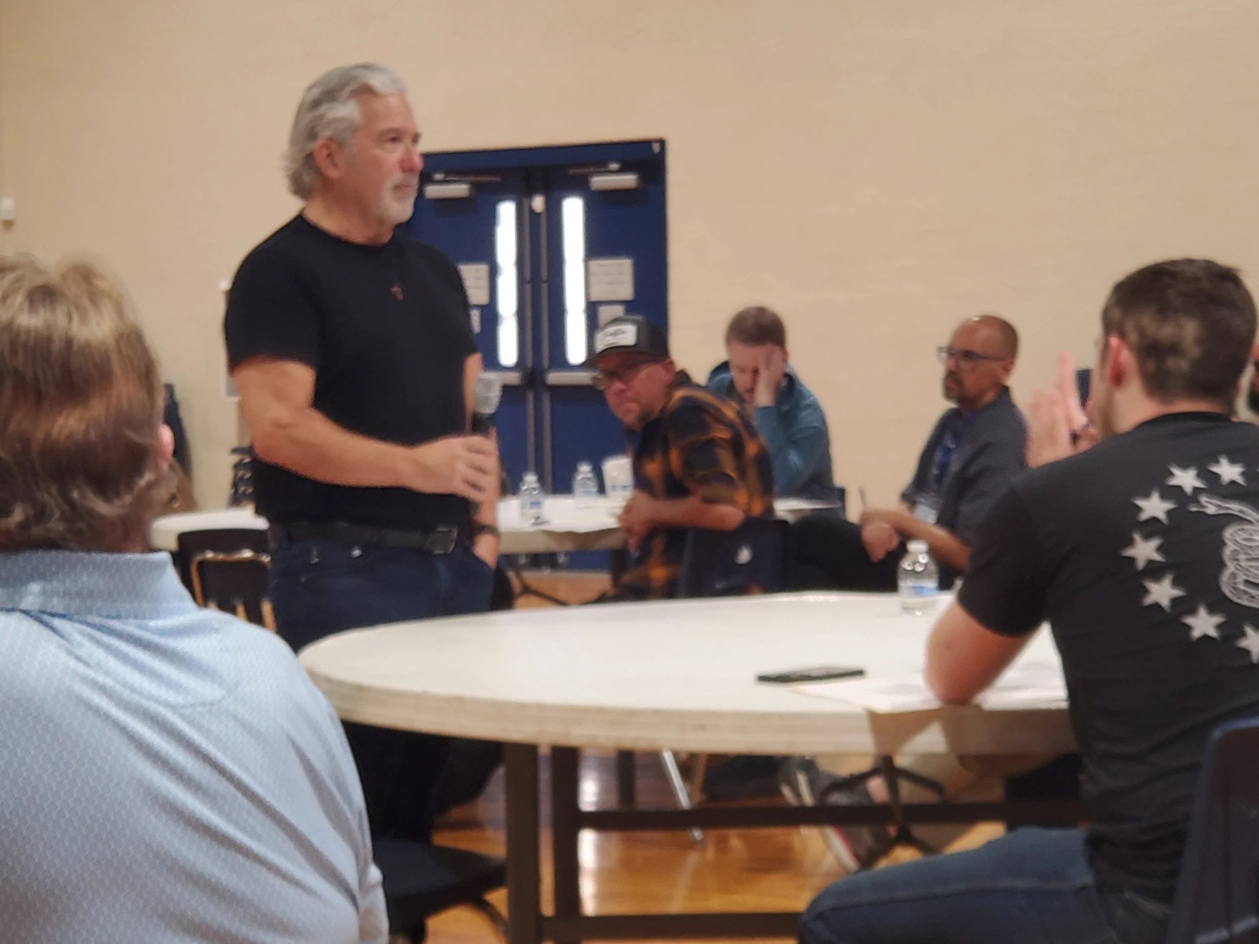 A speaker talking with men at round tables