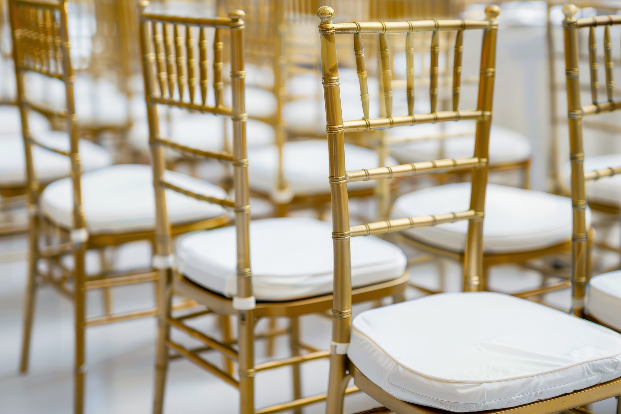 Golden chairs with white cushions arranged in rows, likely at an event or banquet setting.