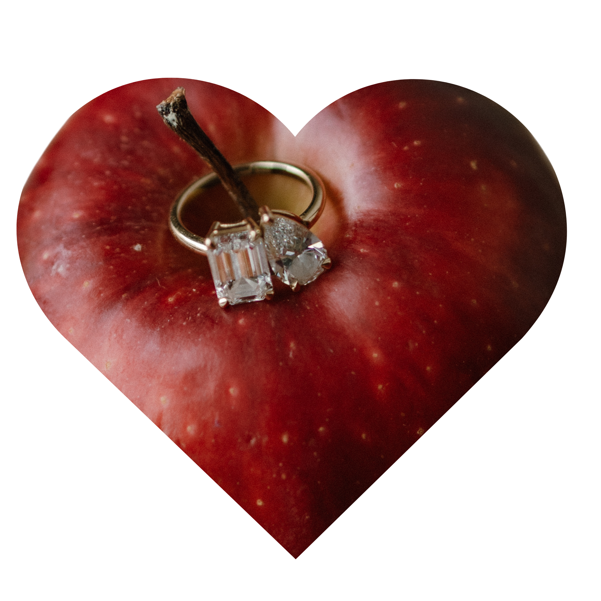 Close-up of a red apple with a small jewelry ring with a diamond at its center, inserted into the apple. The apple has a brown stem and some small yellowish spots.