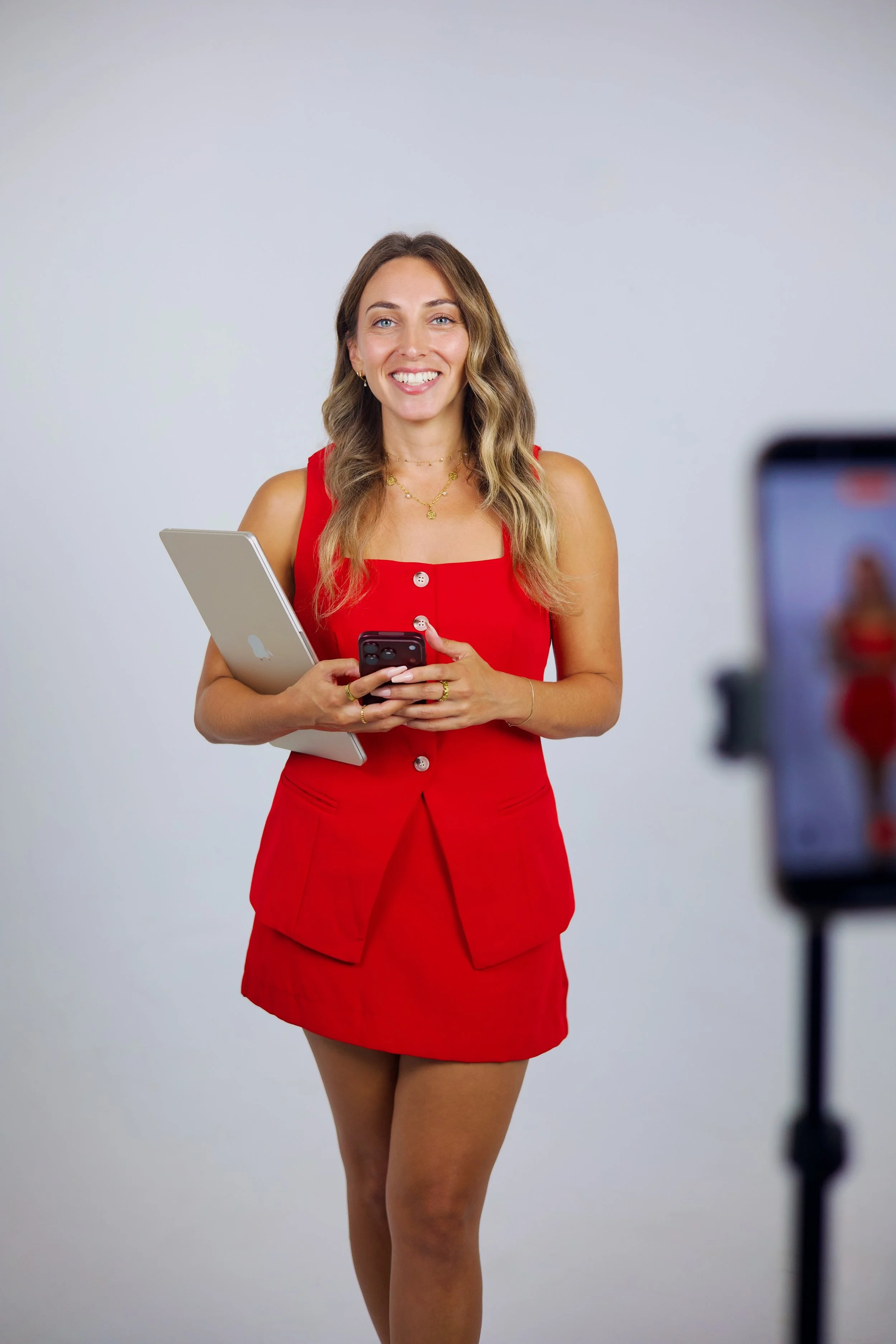 Founder Hannah Kavy, San Diego social media and video content creator, smiling in a red outfit holding a tablet and phone