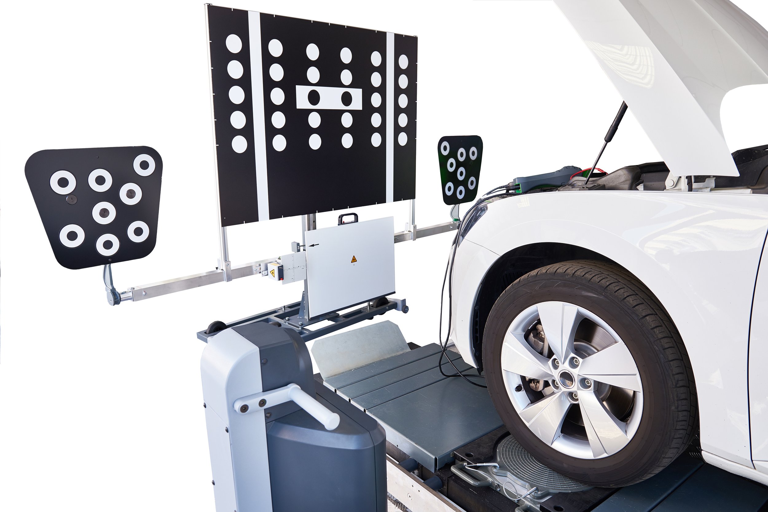 A specialized autonomous vehicle testing setup with a white car, a large black and white target board with circular markers, and smaller target panels, used for calibrating and testing automated driving systems. ADAS.