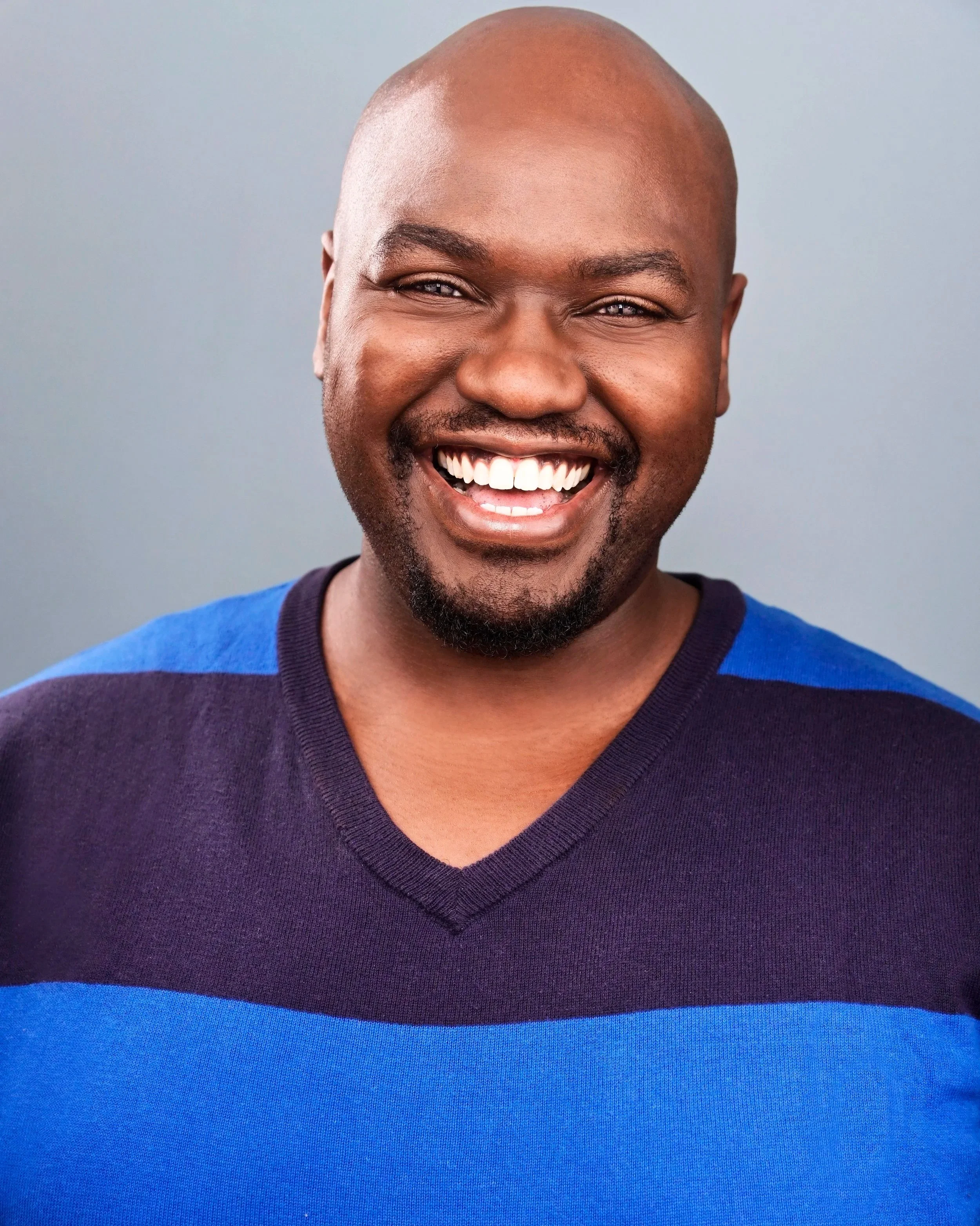 Close-up portrait of a smiling bald Black man with a beard wearing a blue and purple shirt