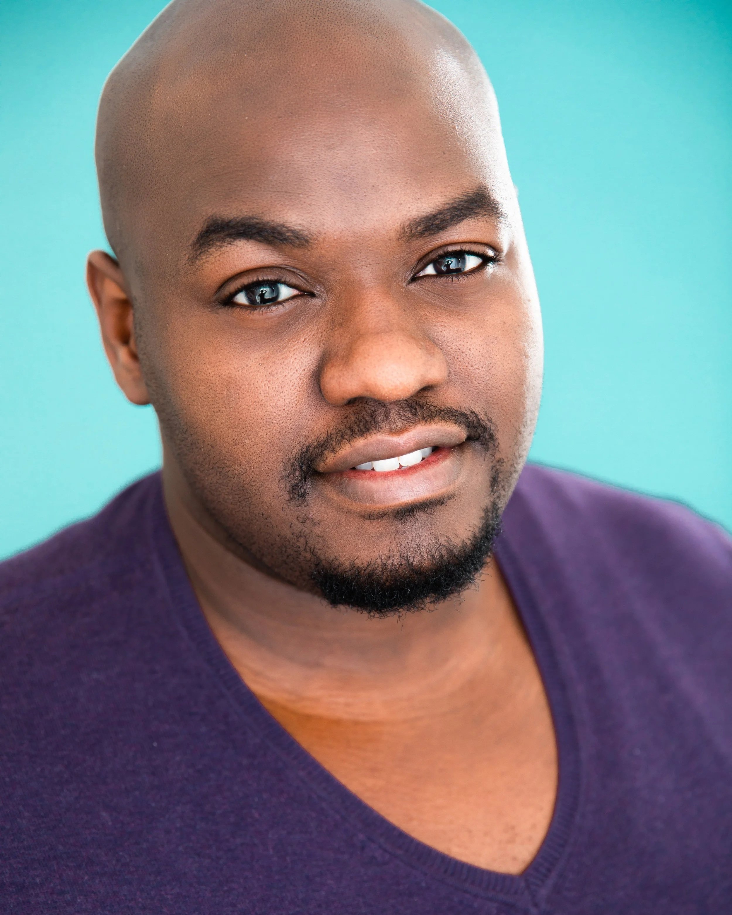 Close-up portrait of a smiling bald Black man with a beard against a turquoise background
