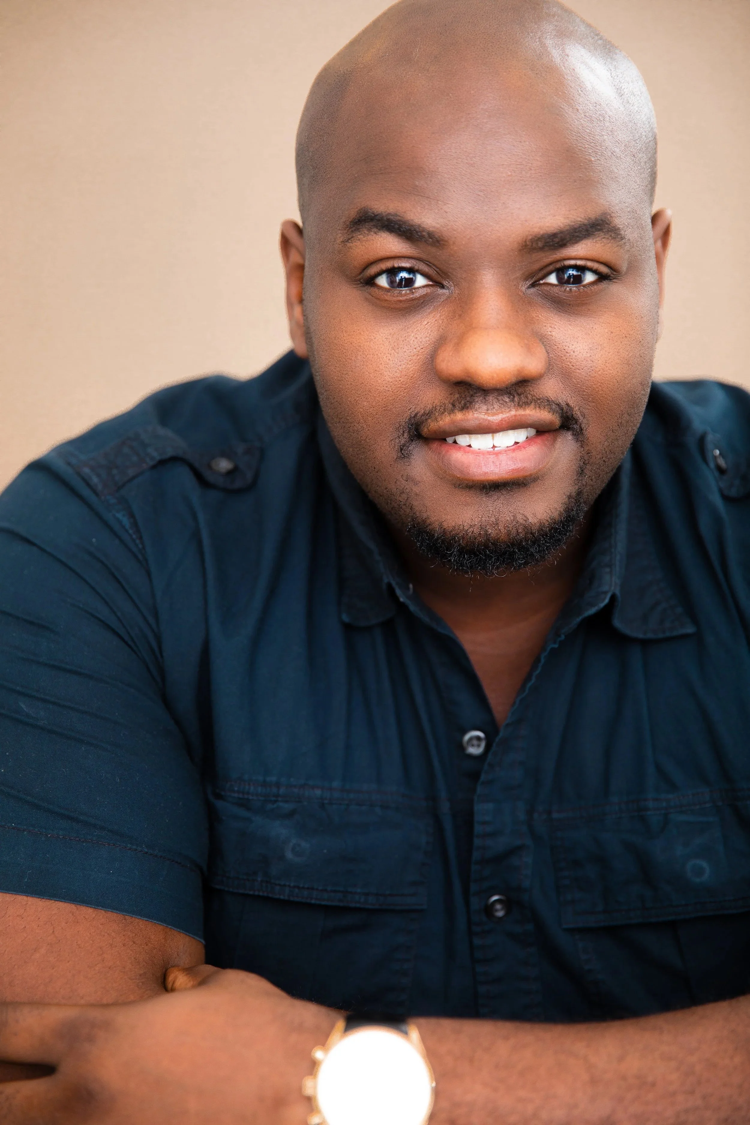 Smiling bald Black man with a beard wearing a dark blue shirt and wristwatch