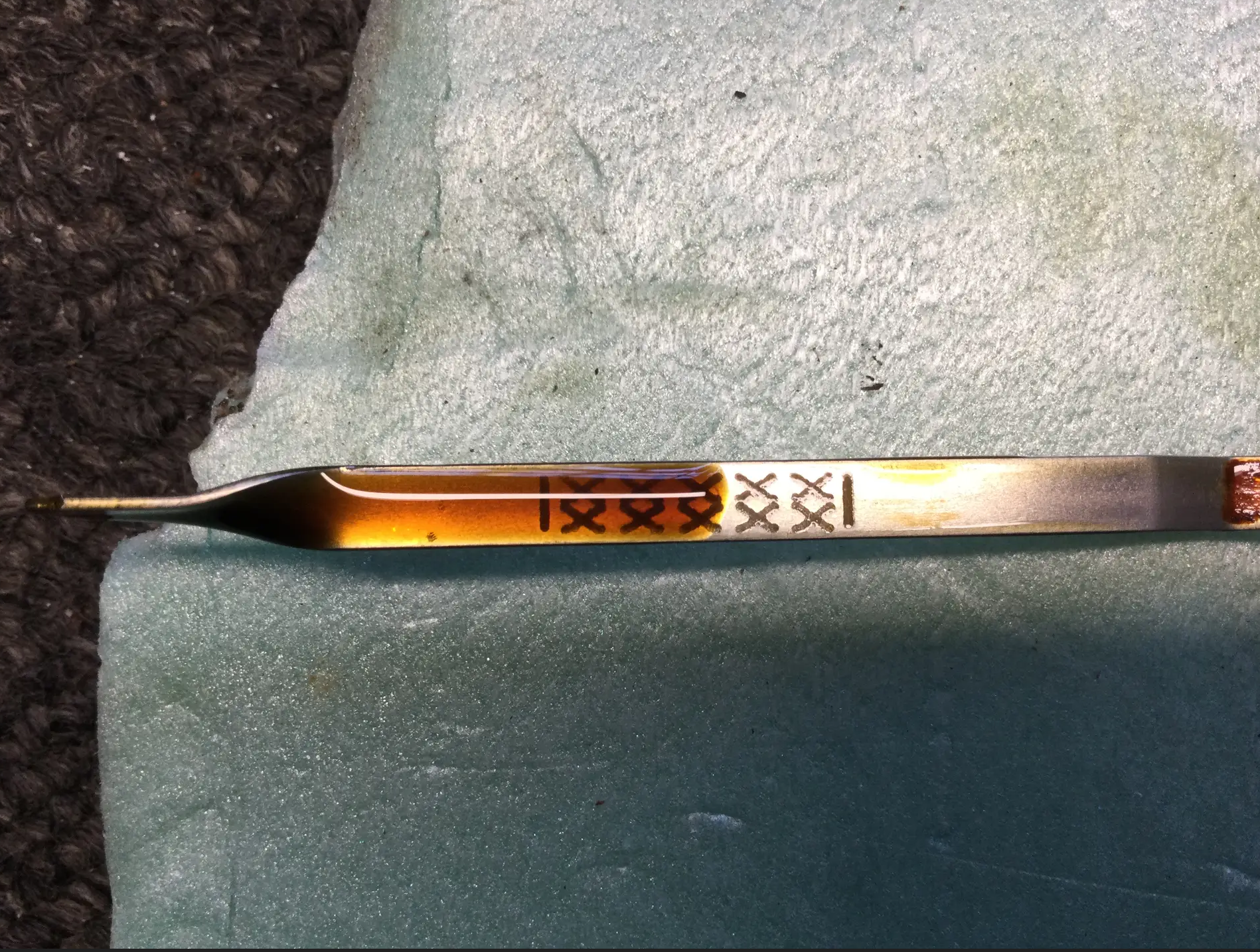 Close-up of a metallic knife with a decorative handle resting on a textured green surface with a corner of a dark brown woven fabric.