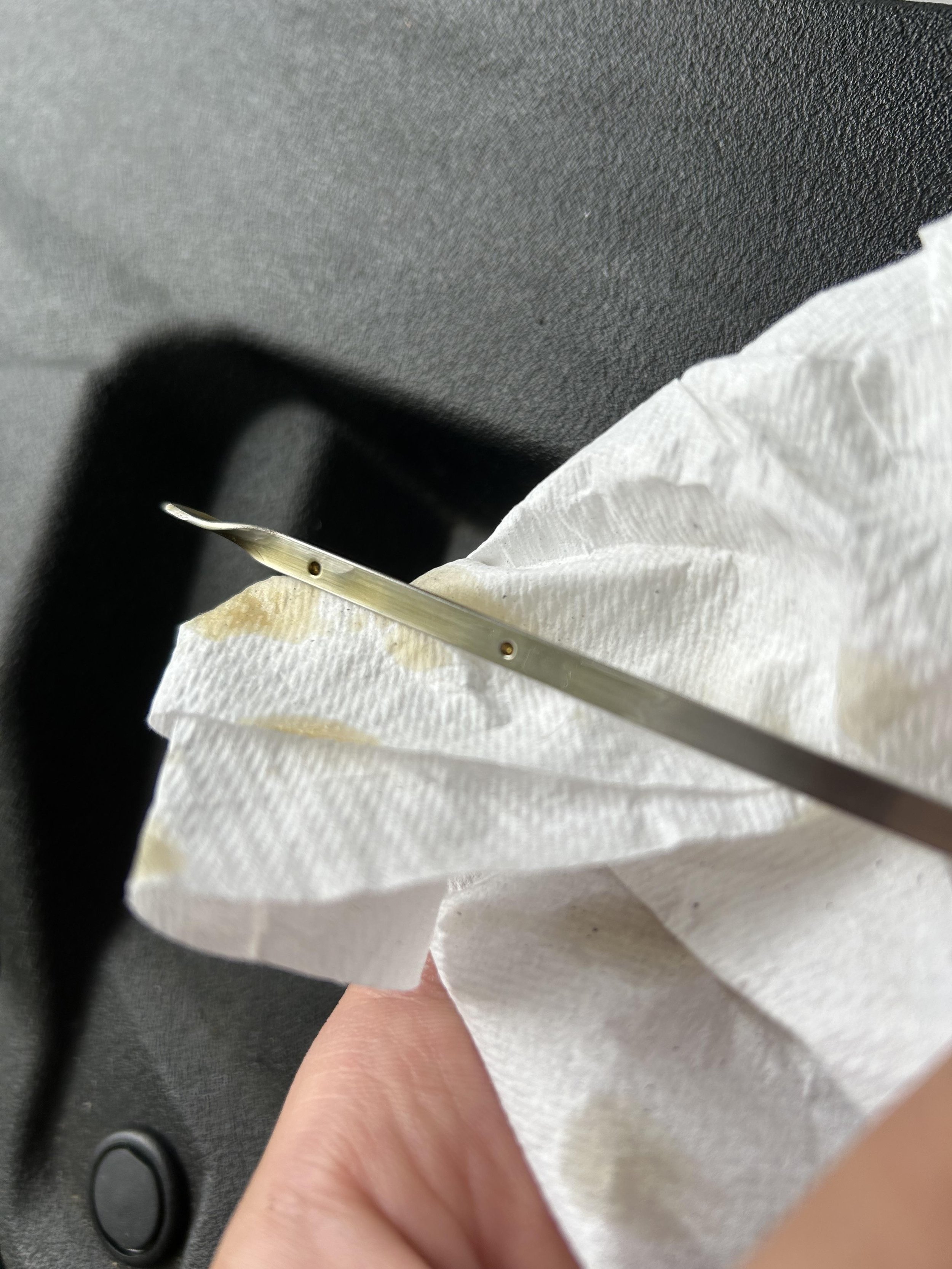 Close-up of a person's finger holding a metal crochet hook surrounded by a white cloth or paper towel, against a dark background.