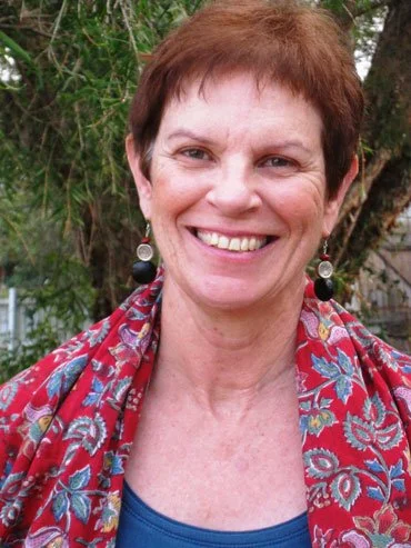 A woman with short brown hair smiling outdoors, wearing a patterned red and blue scarf and earrings.
