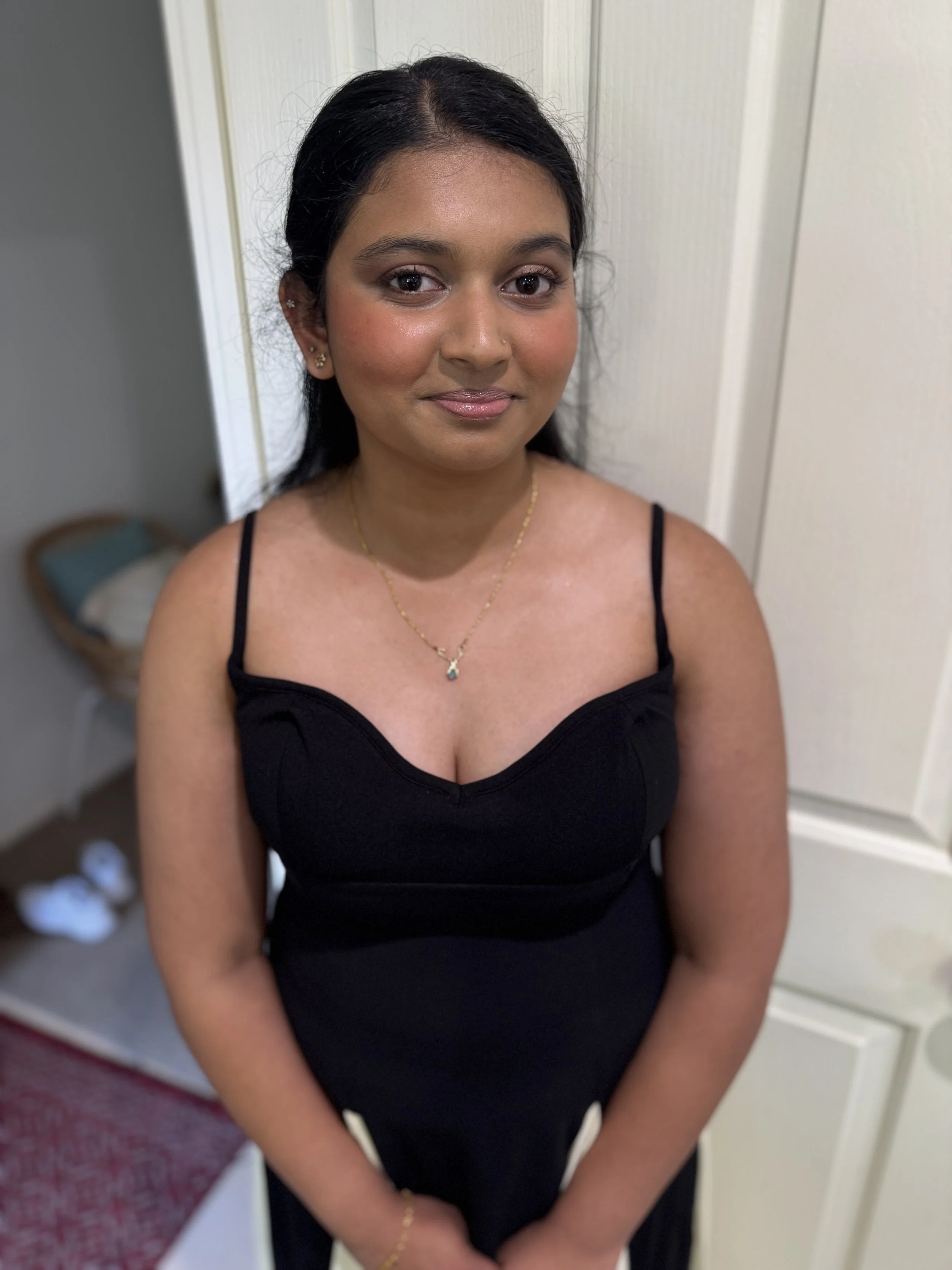 Portrait of a smiling woman with dark hair, gold jewelry, and a black sleeveless top indoors