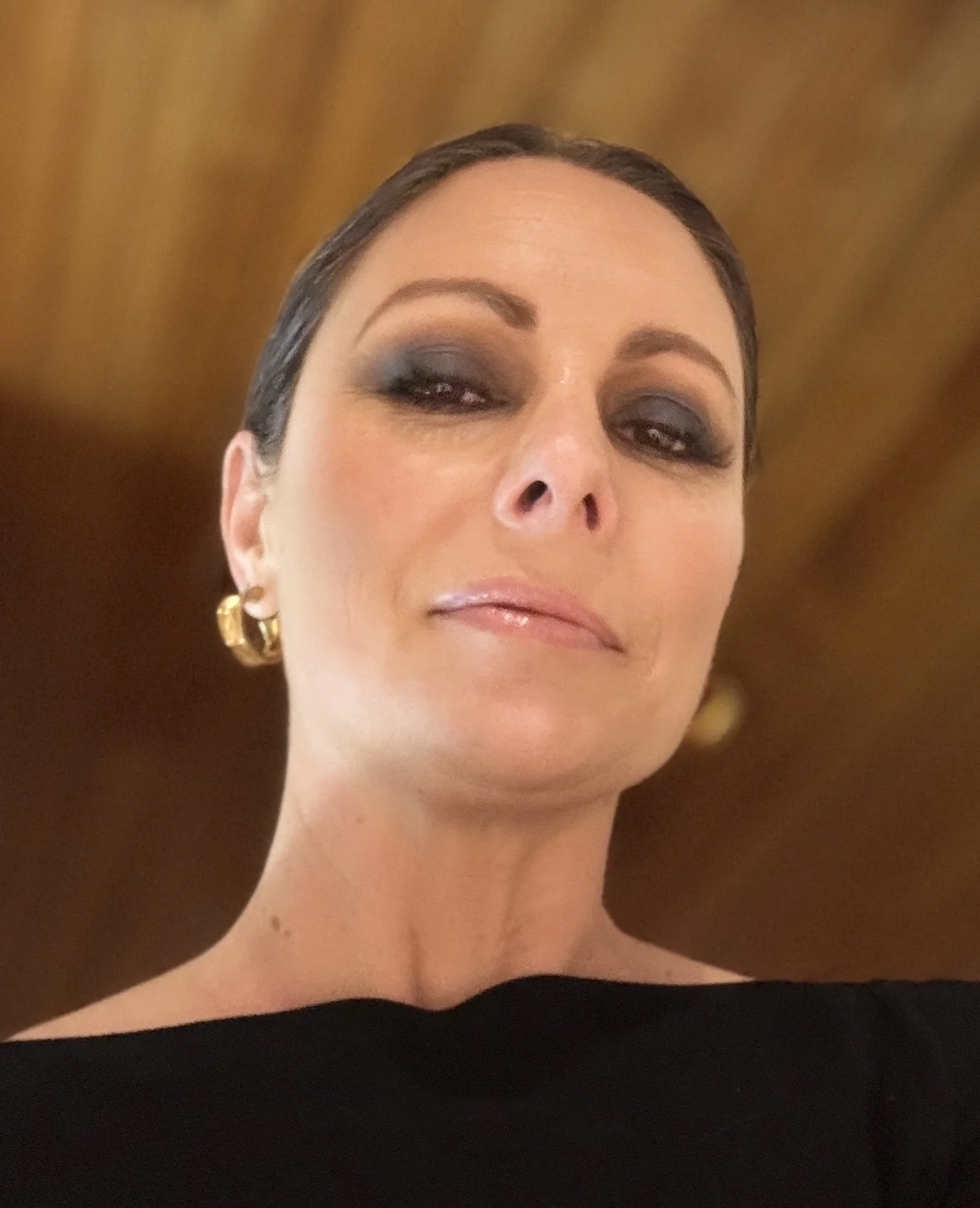 Close-up portrait of a woman with smoky eye makeup, gold hoop earrings, and a black off-the-shoulder top.