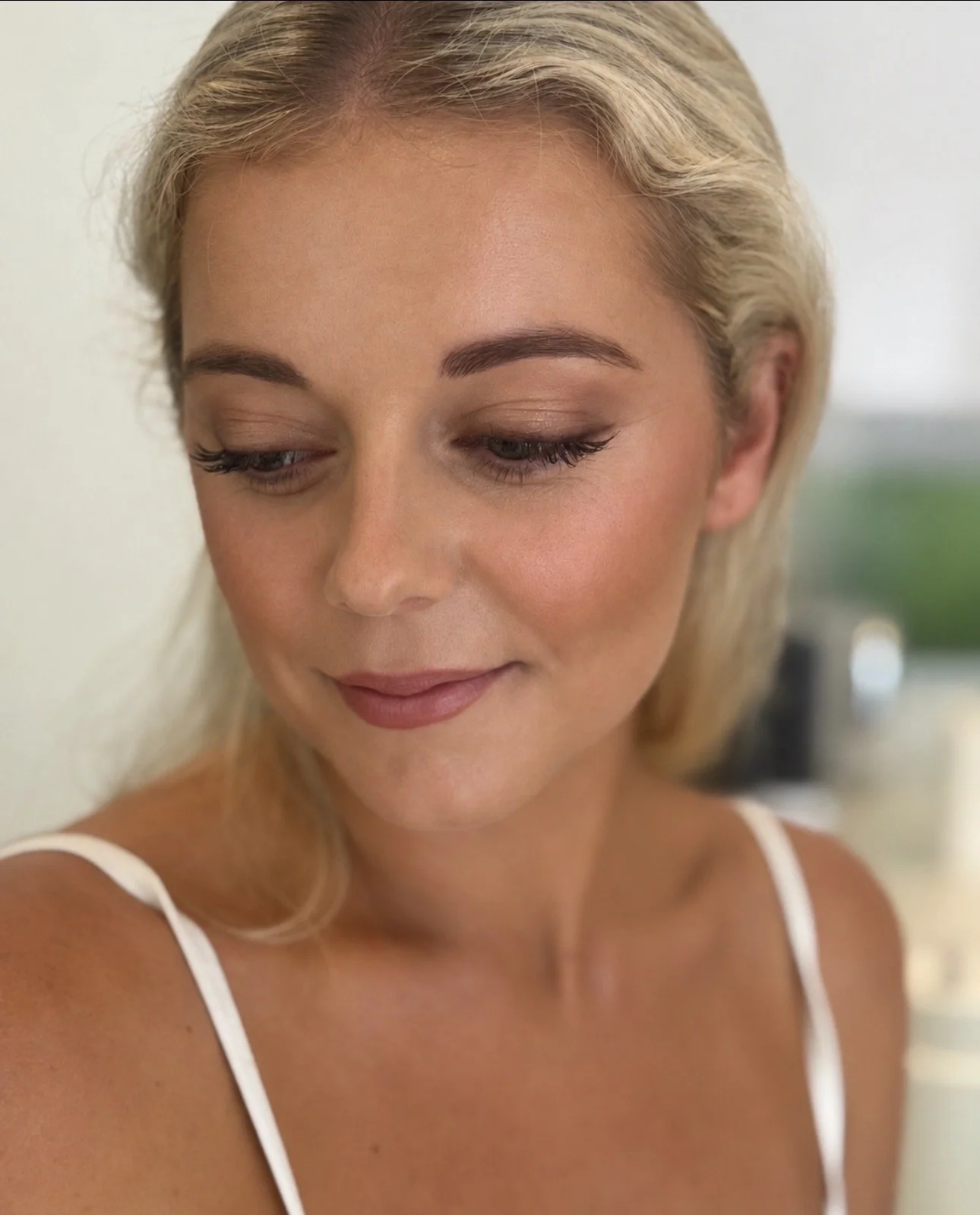 Close-up portrait of a blonde woman with closed eyes wearing a white tank top