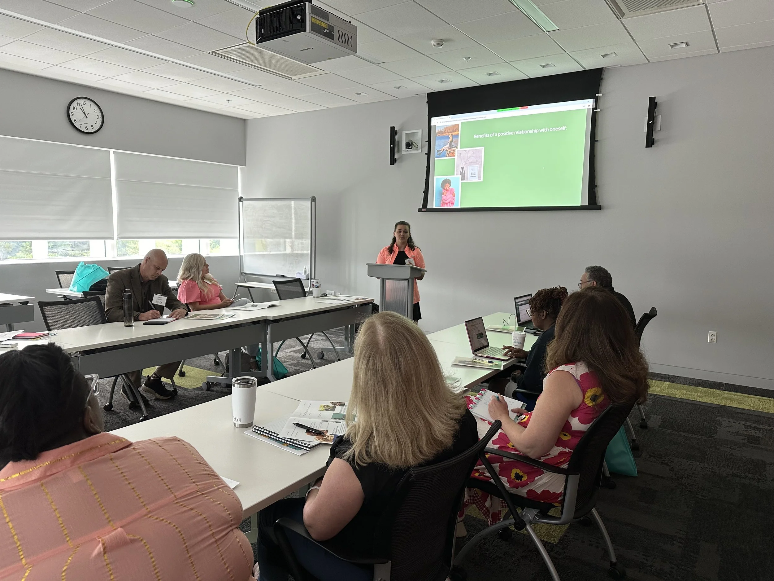Woman presenting a positive self-relationship workshop to attendees in a modern conference room