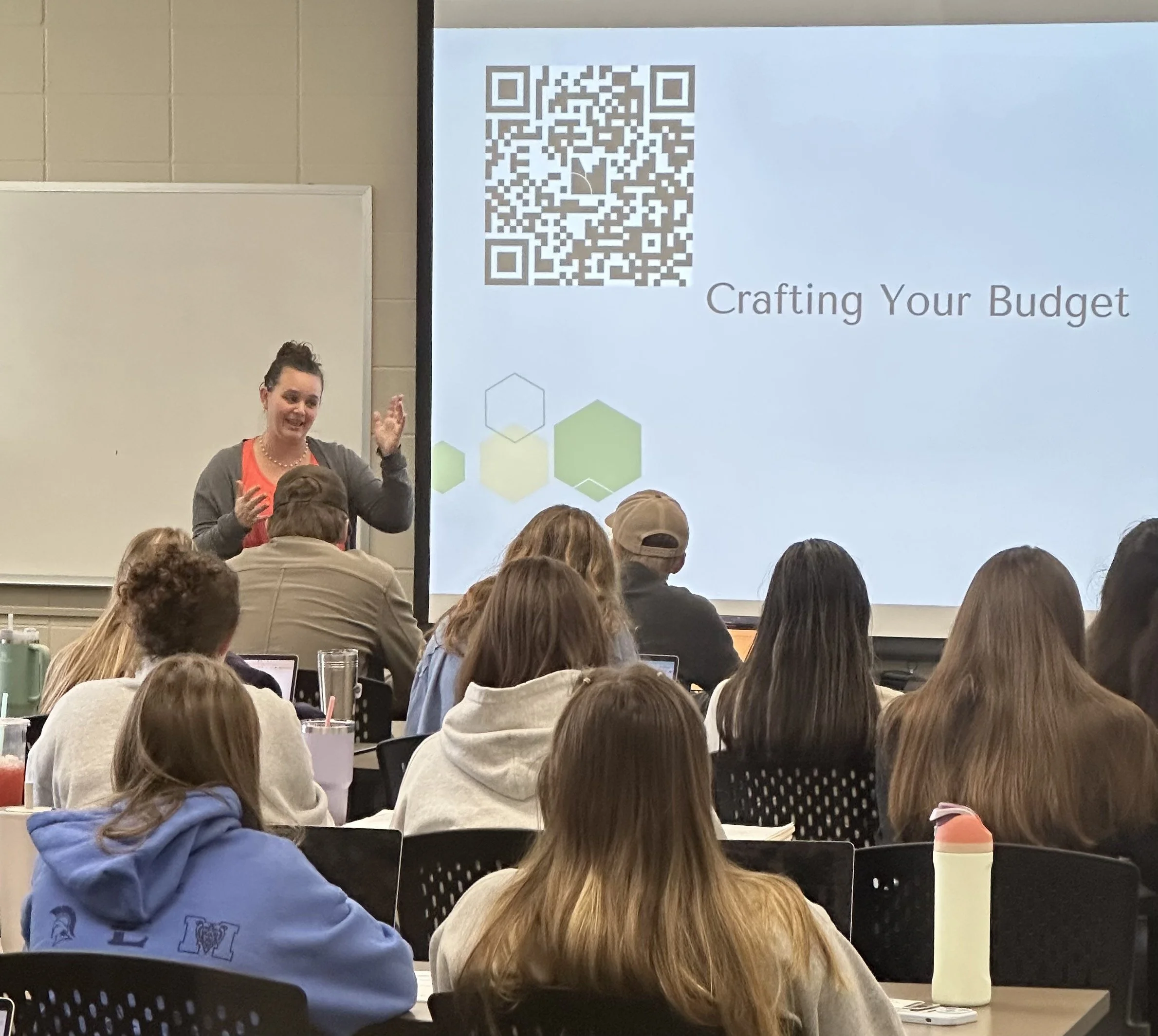 Speaker presenting a “Crafting Your Budget” slide with a QR code to an audience in a classroom.