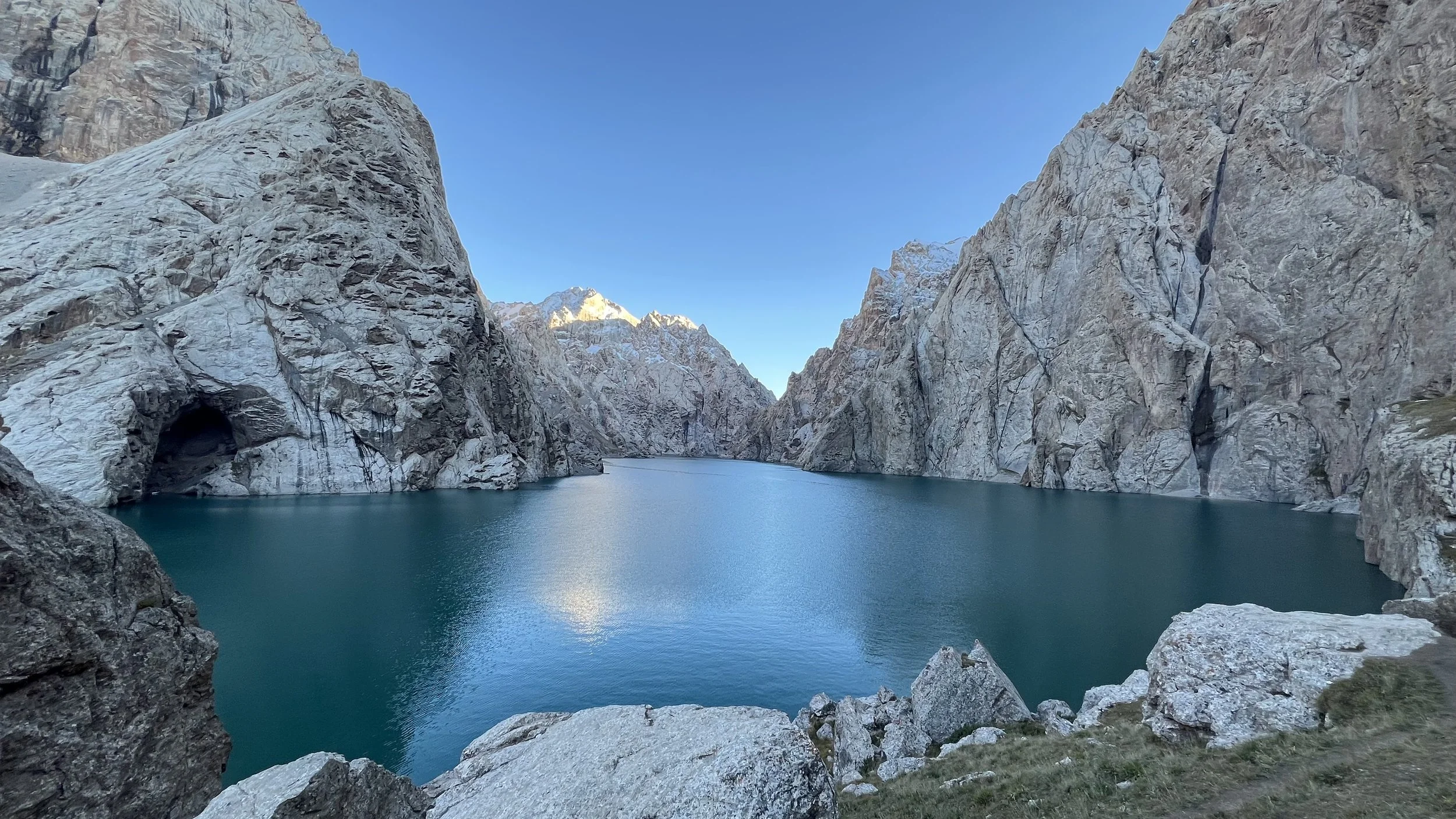 A mountain landscape with a body of water surrounded by tall, rocky cliffs under a clear blue sky.