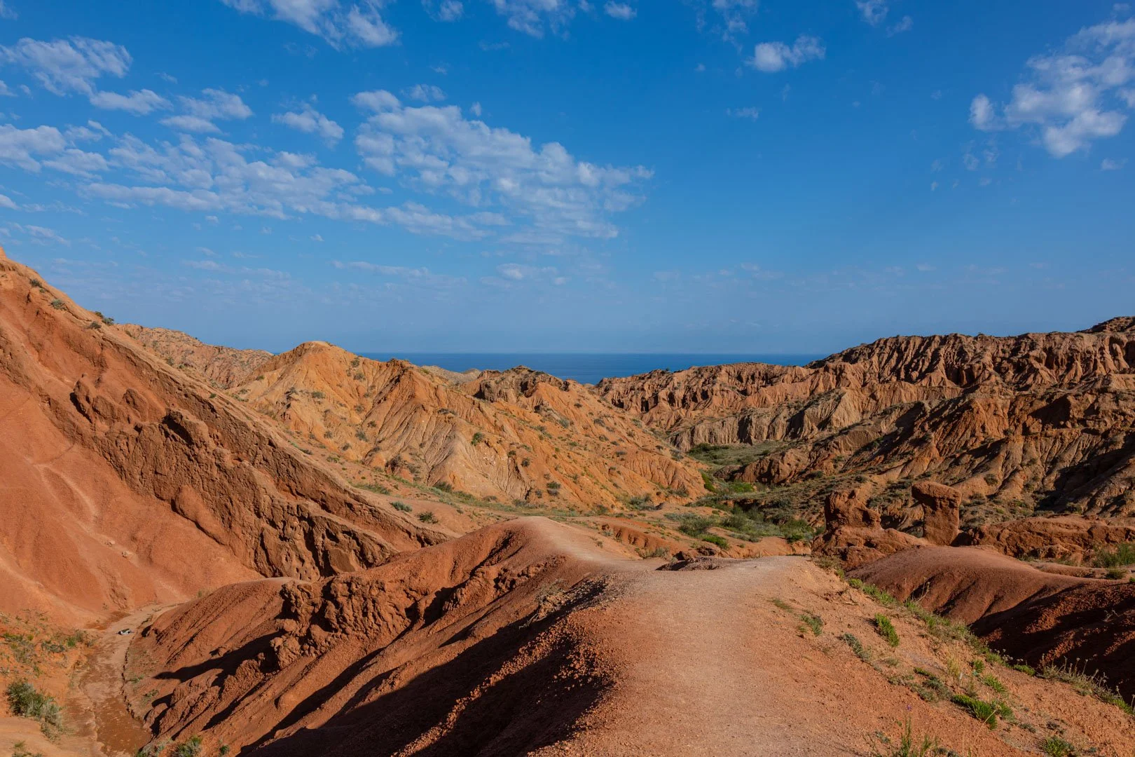 Desert landscape with colorful, layered rocky hills and a blue sky with scattered clouds.
