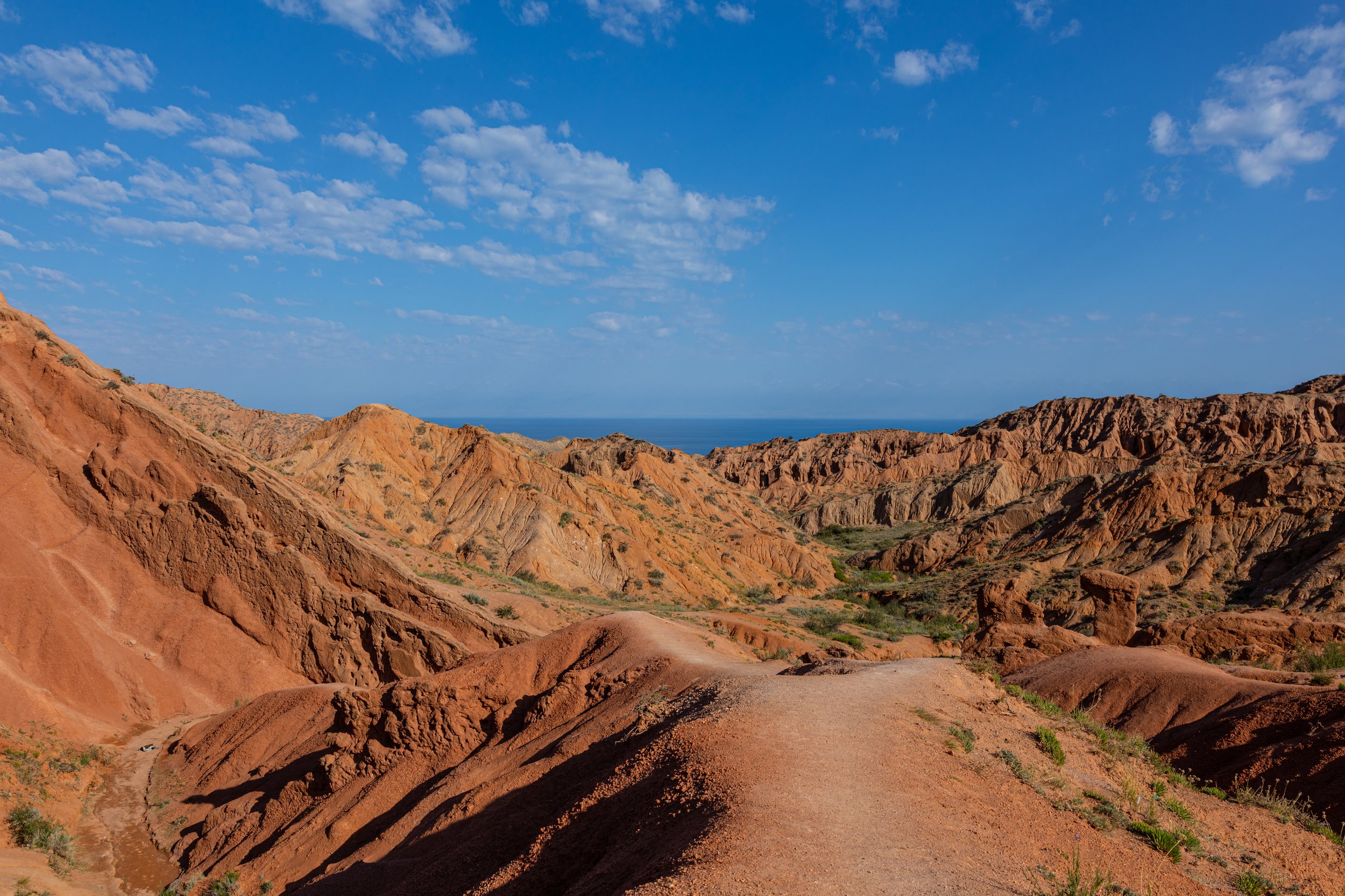Arid, reddish-orange desert hills under a blue sky with scattered white clouds.