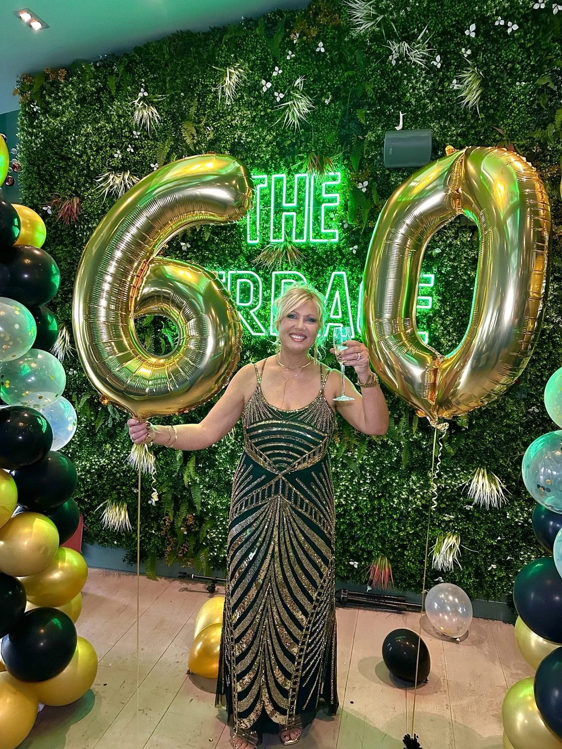 Woman celebrating her 60th birthday in a black and gold gown, surrounded by gold balloons and party decorations, featured in Love, Blair's event portfolio.