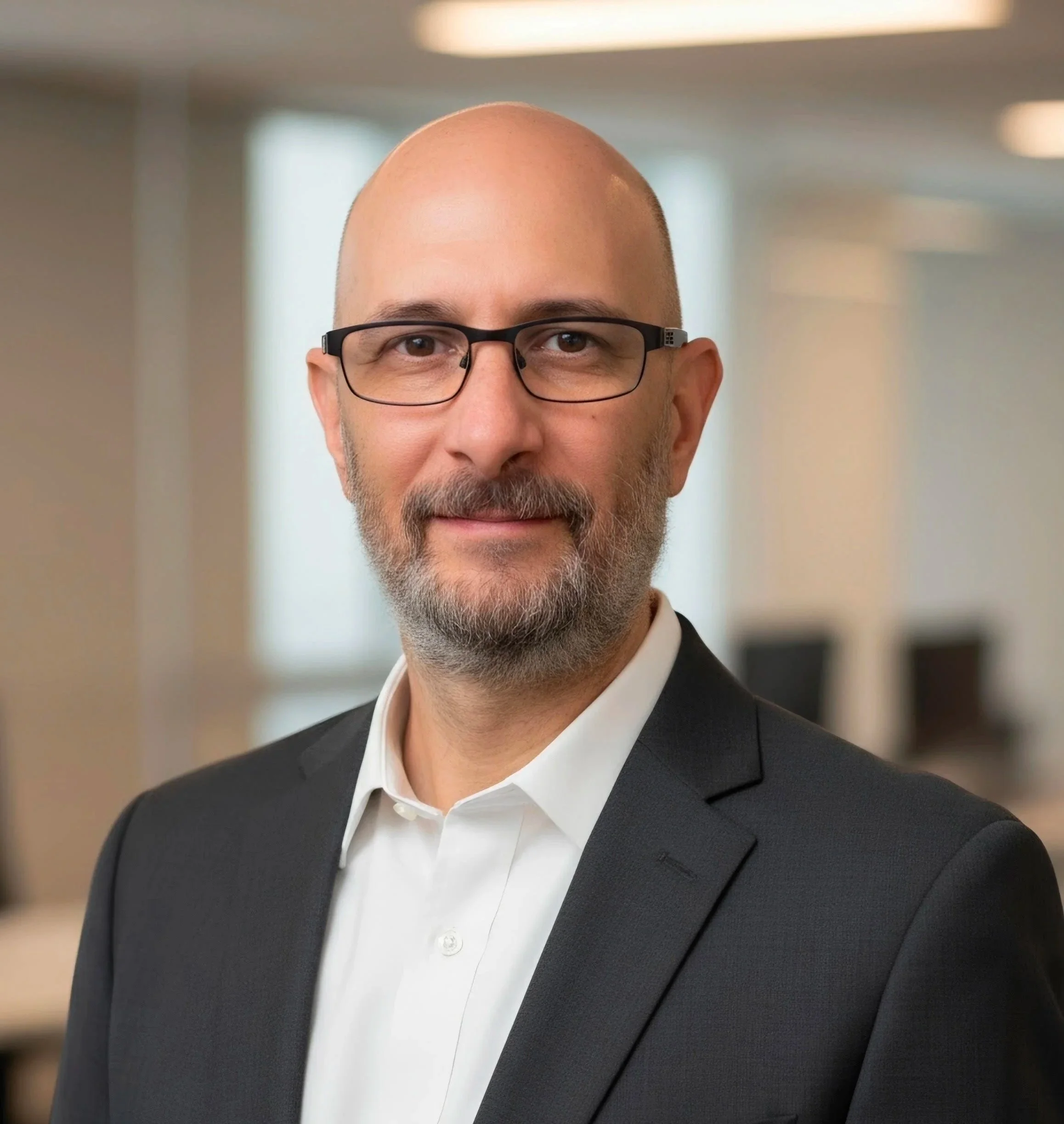 Professional headshot of a bald, bearded man wearing glasses, a dark suit, and white shirt