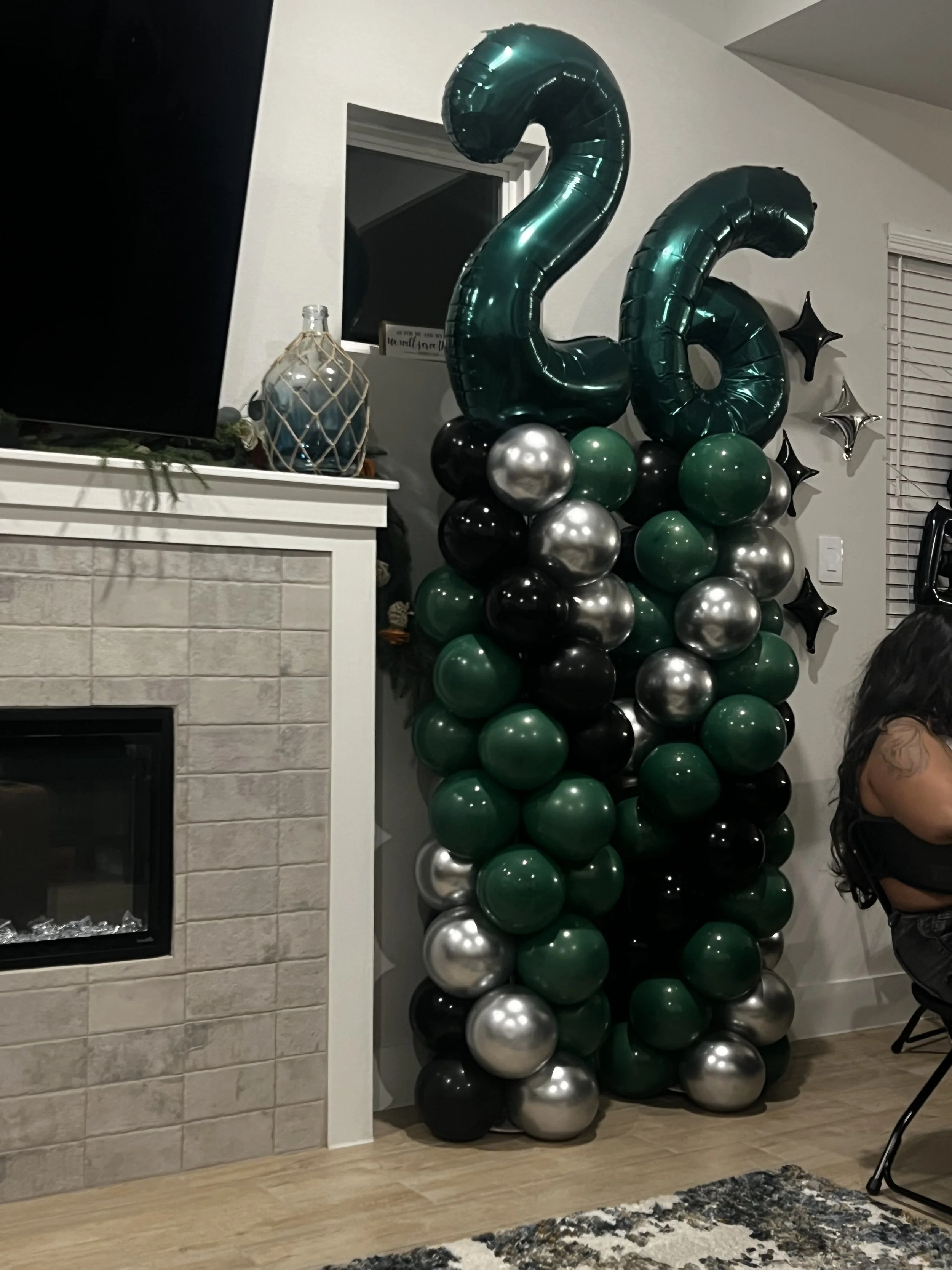 Large green, black, and silver balloon sculpture shaped like a seahorse beside a fireplace.