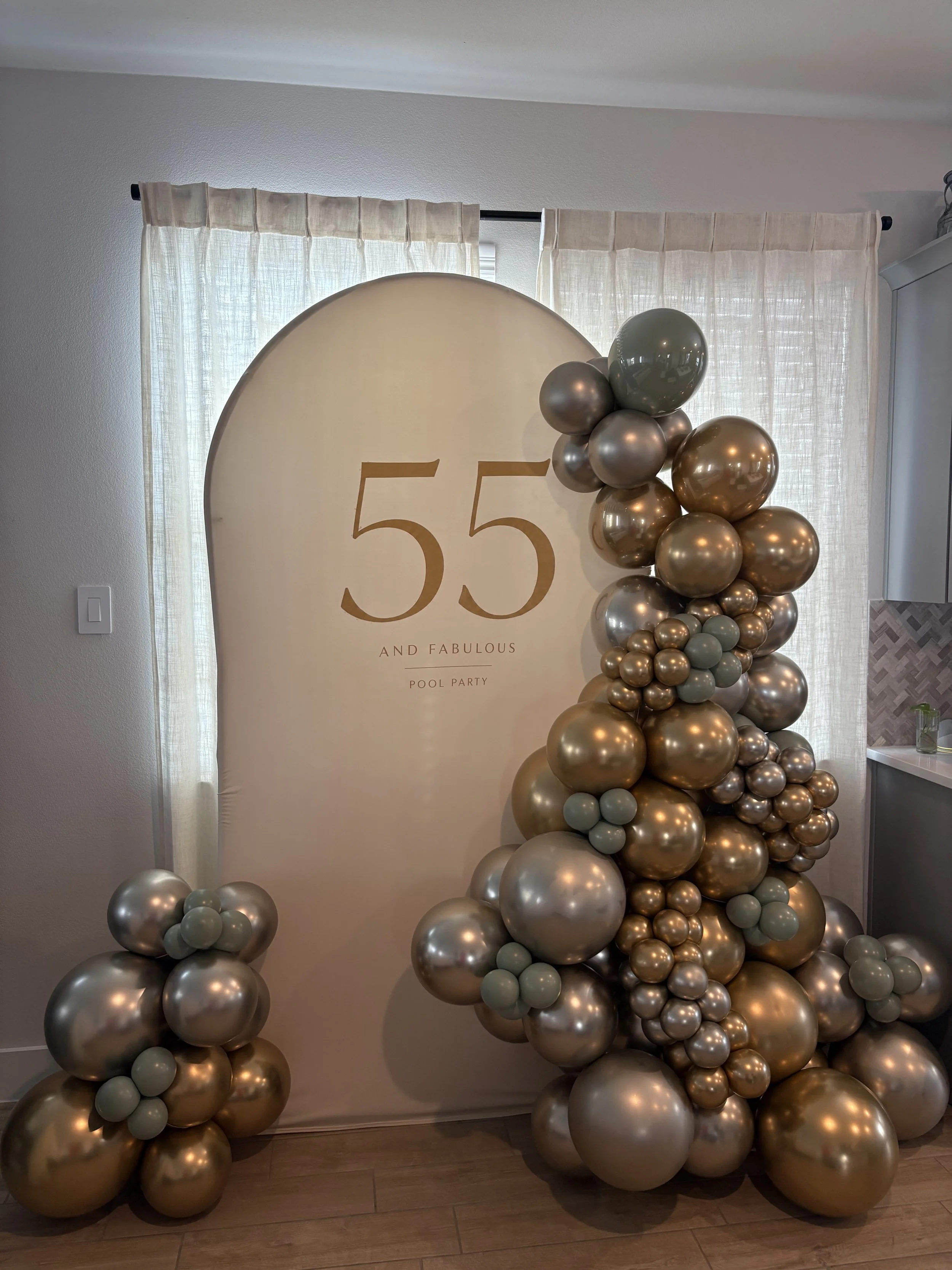 Elegant 55th birthday party backdrop with gold lettering, metallic balloon garland, and matching balloon clusters.