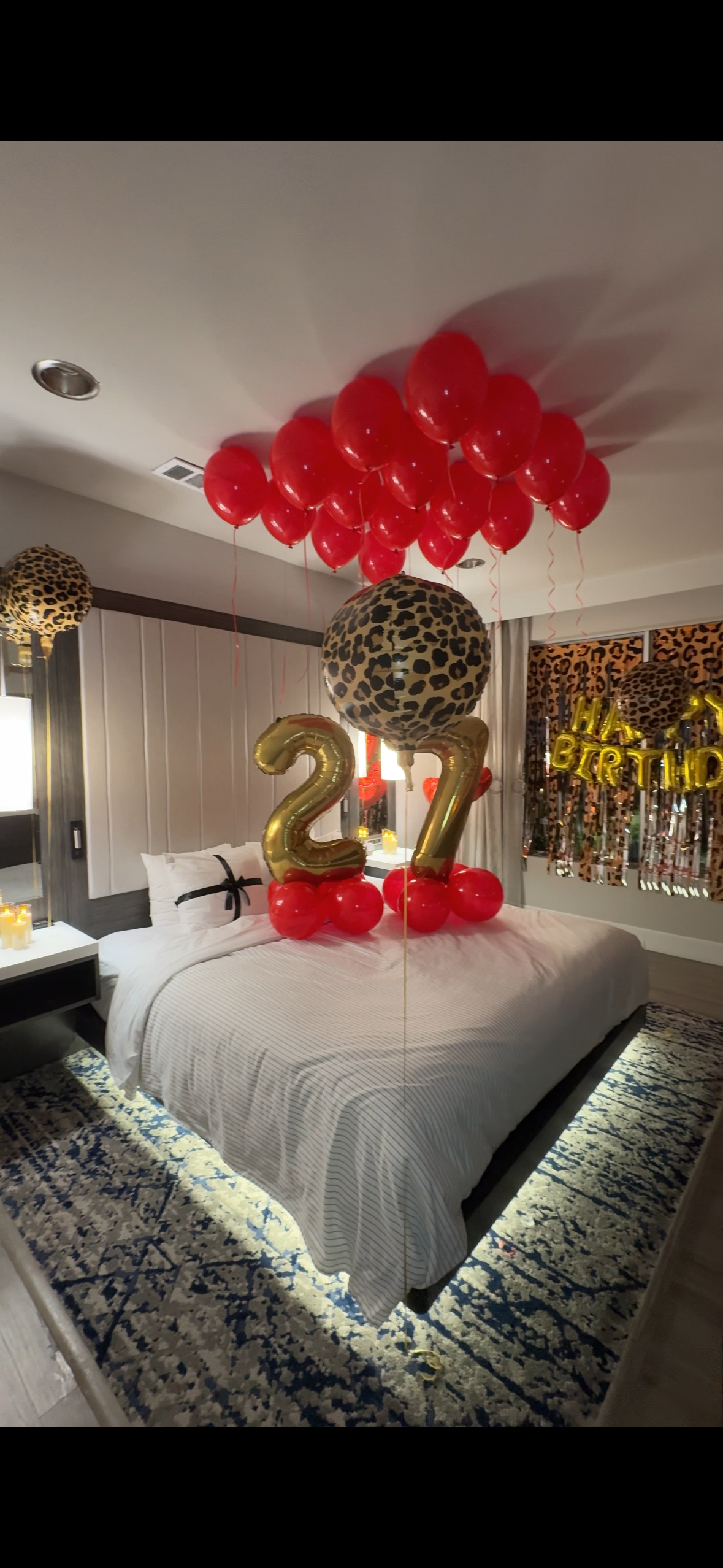 Hotel bedroom decorated for a 27th birthday with red balloons, gold number balloons, leopard-print balloons, and a birthday banner.