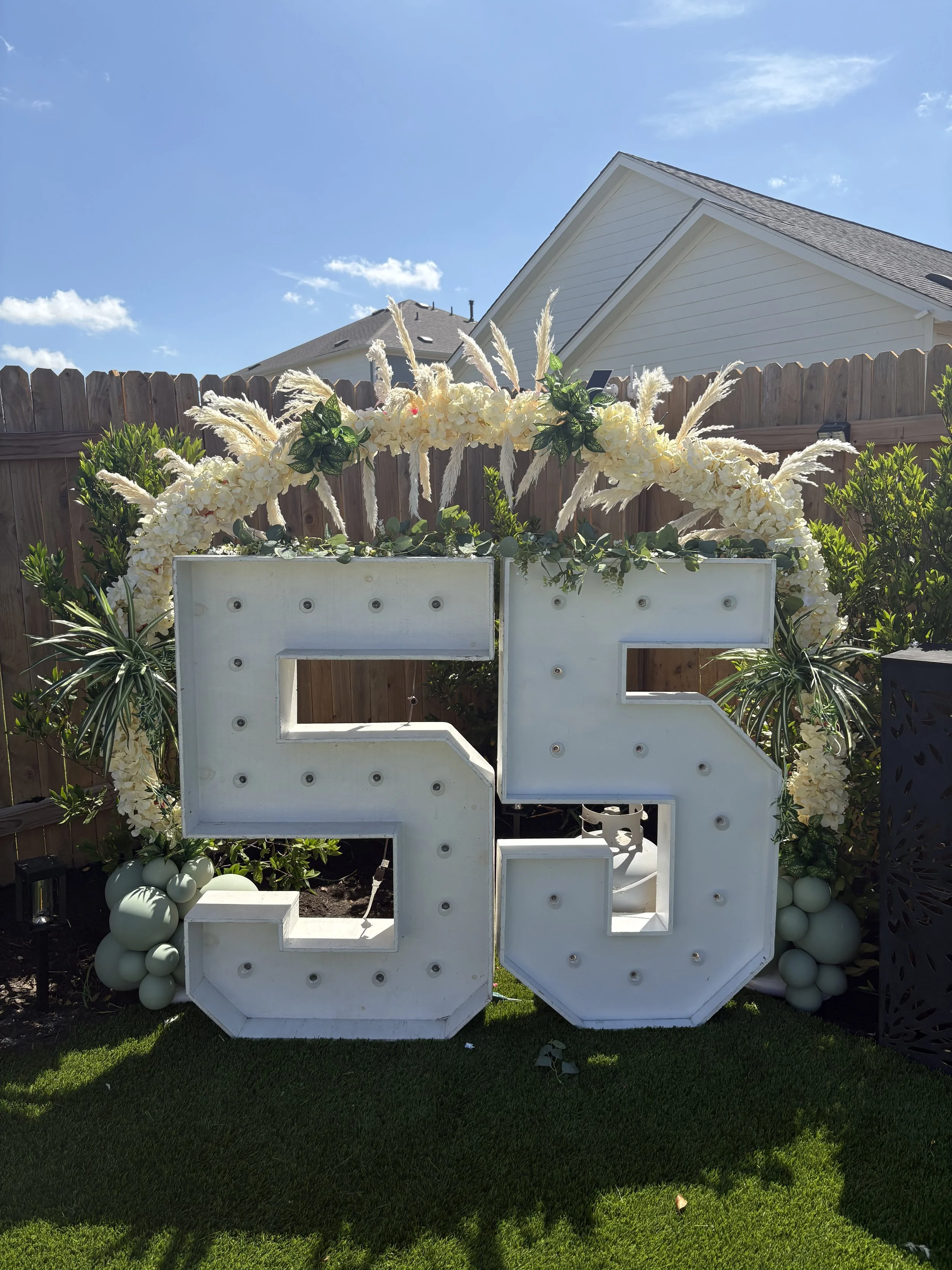 Large white outdoor marquee letters decorated with cream flowers and pampas grass on a lawn.