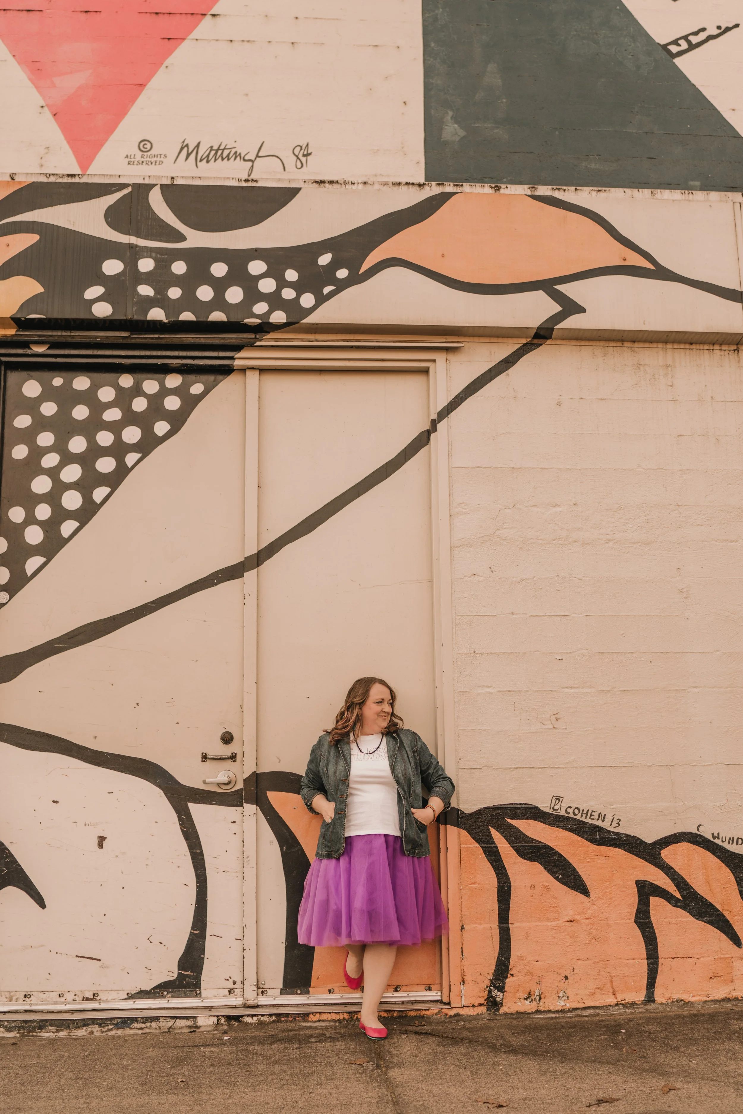 Artist standing against a freight door with a part of a mural on the wall