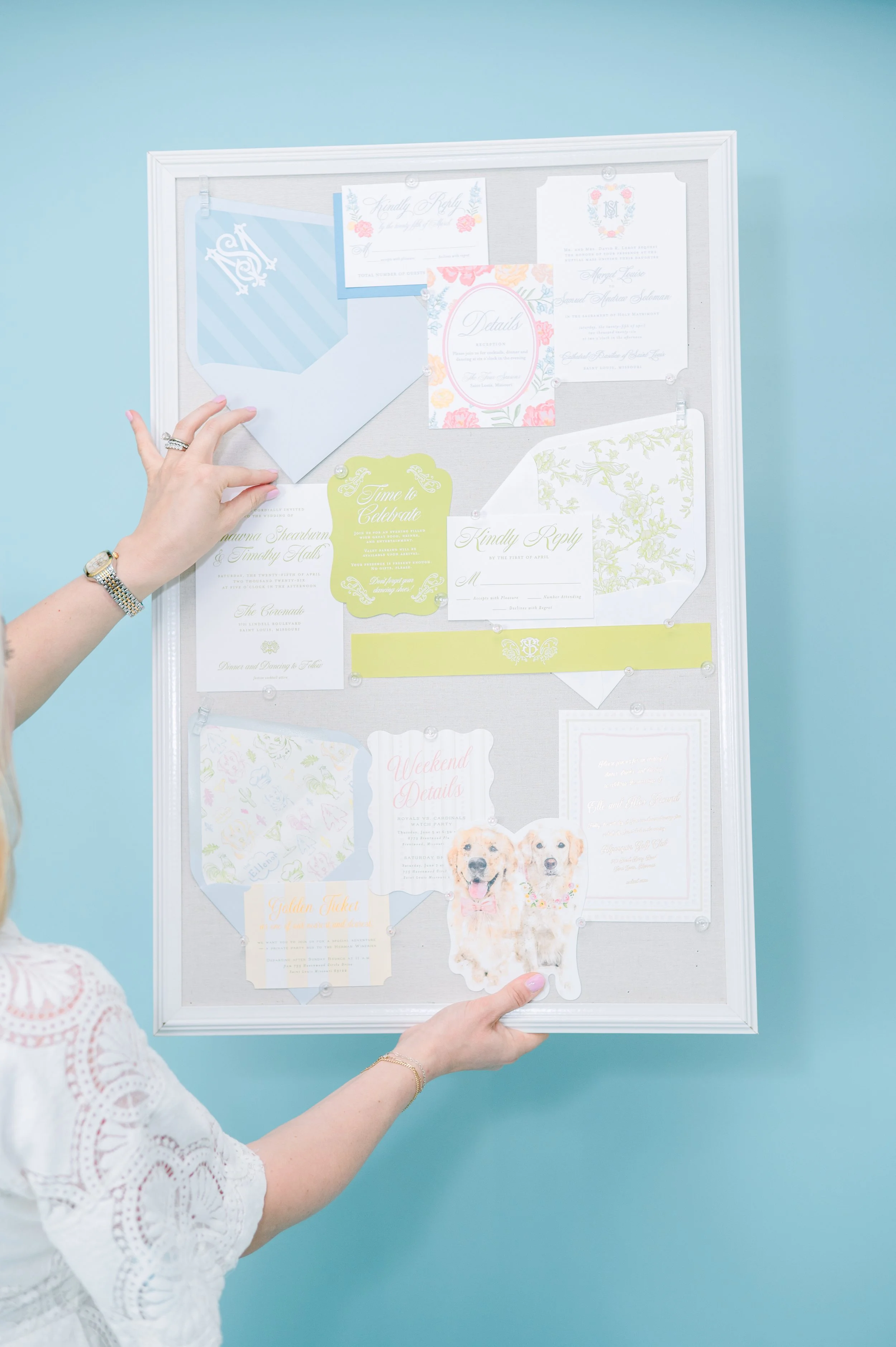 Person holding a decorative wedding or event notice board with unrelated papers and cards attached, against a light blue wall.