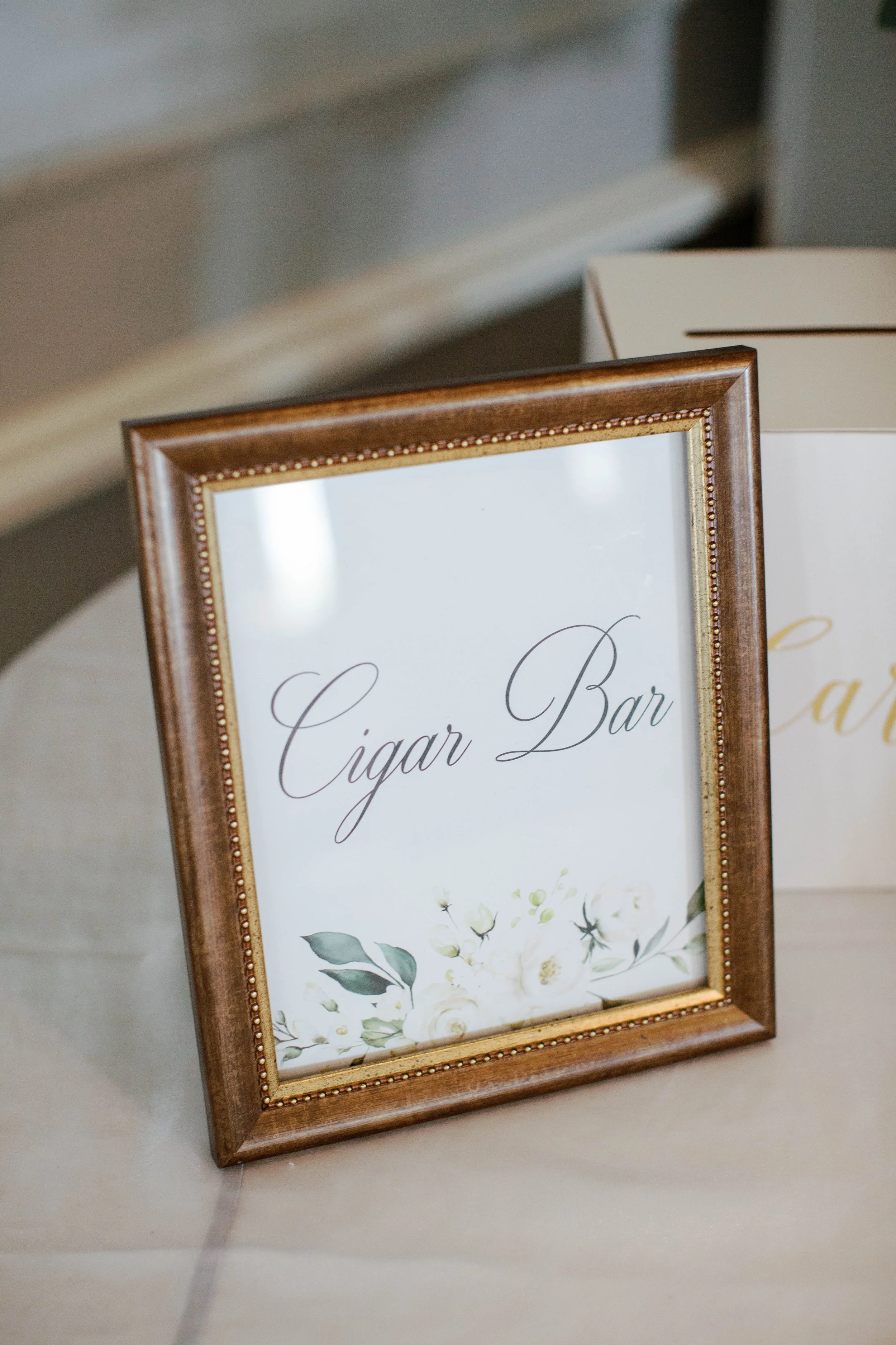 Wooden framed sign with floral design and cursive text reading "Cigar Bar."