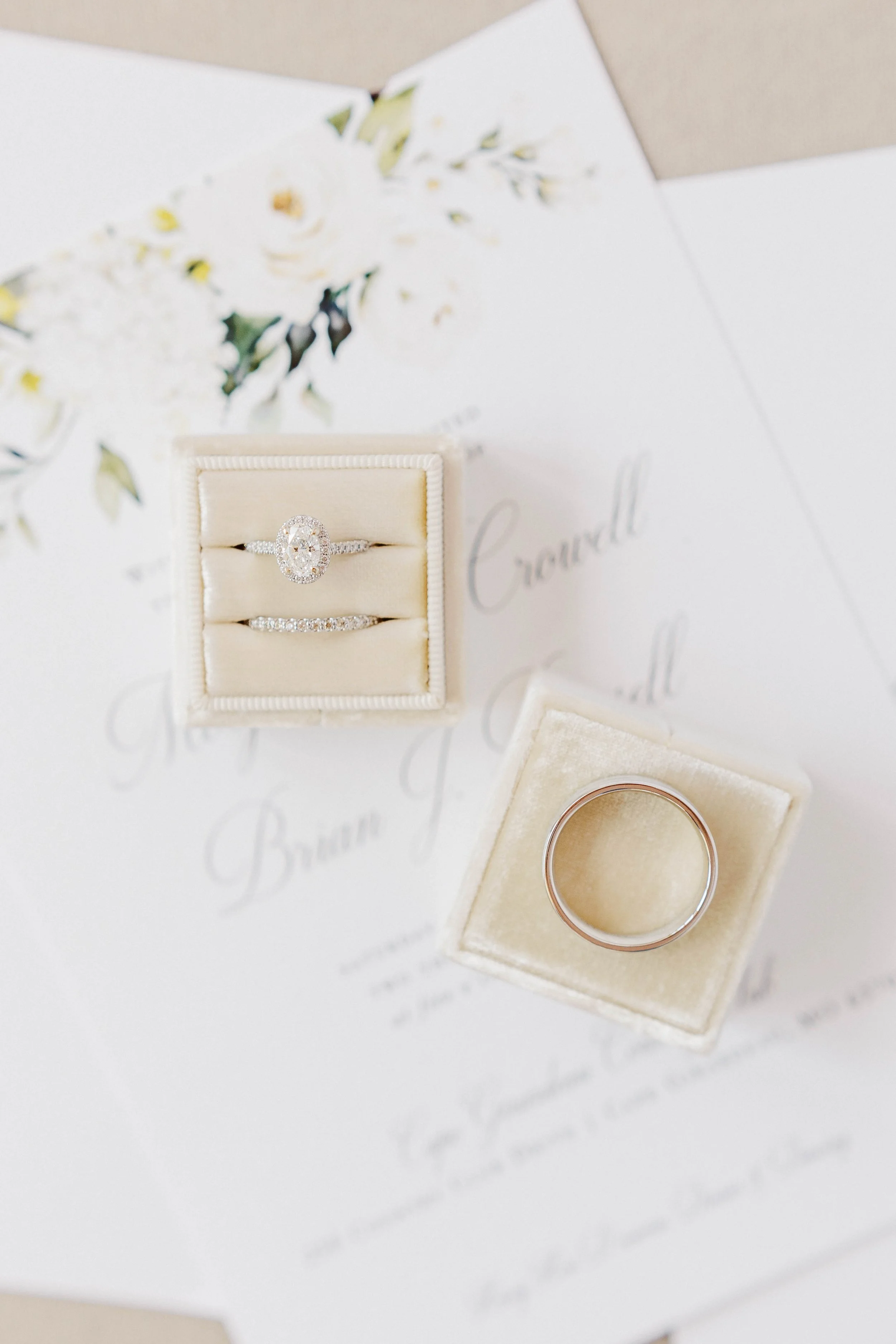 A jewelry box with an engagement ring and wedding band on top of a white card with floral designs.