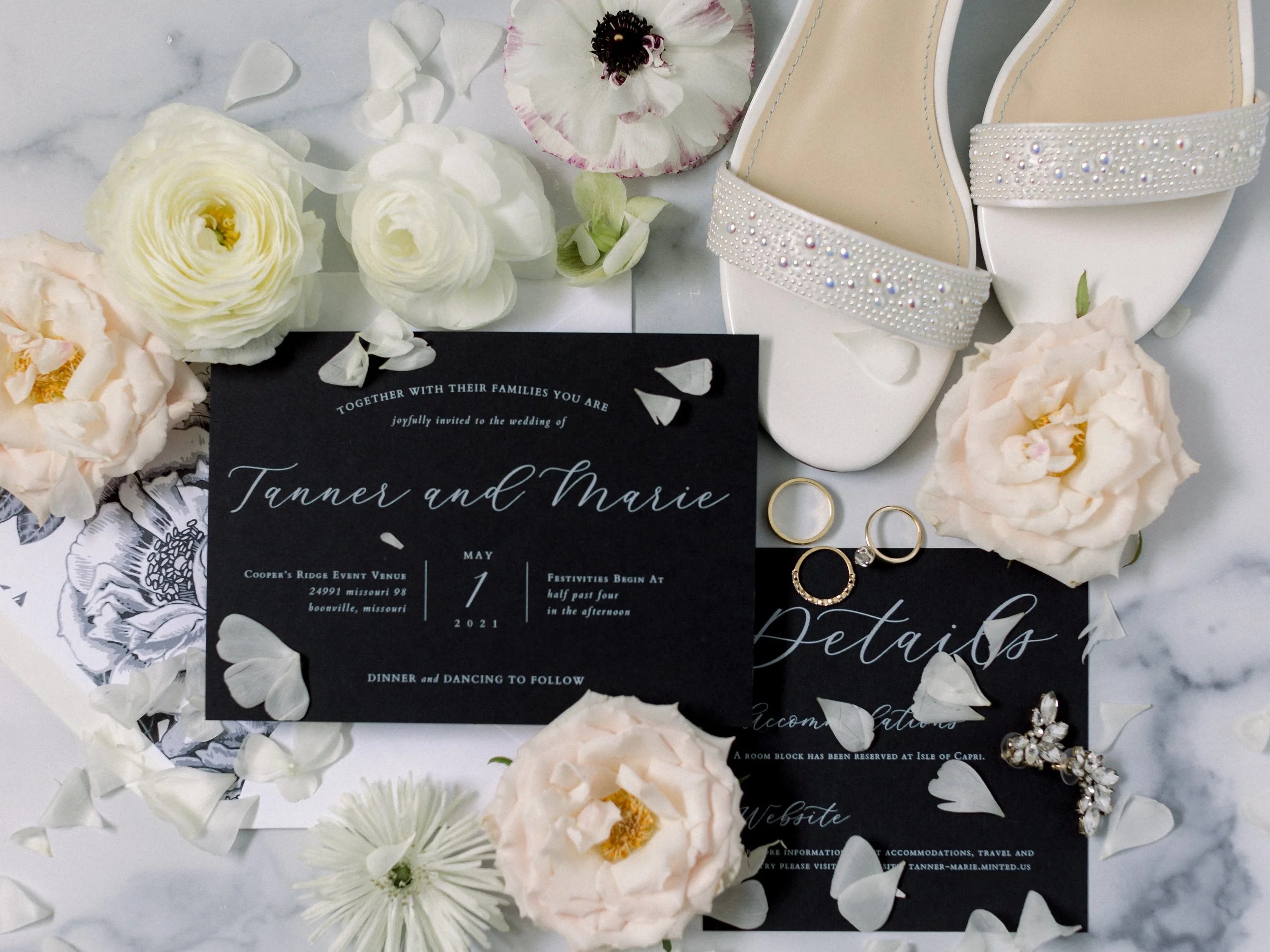 Wedding invitation surrounded by white and soft pink flowers and jewelry, with white high-heeled shoes decorated with pearls and rhinestones.