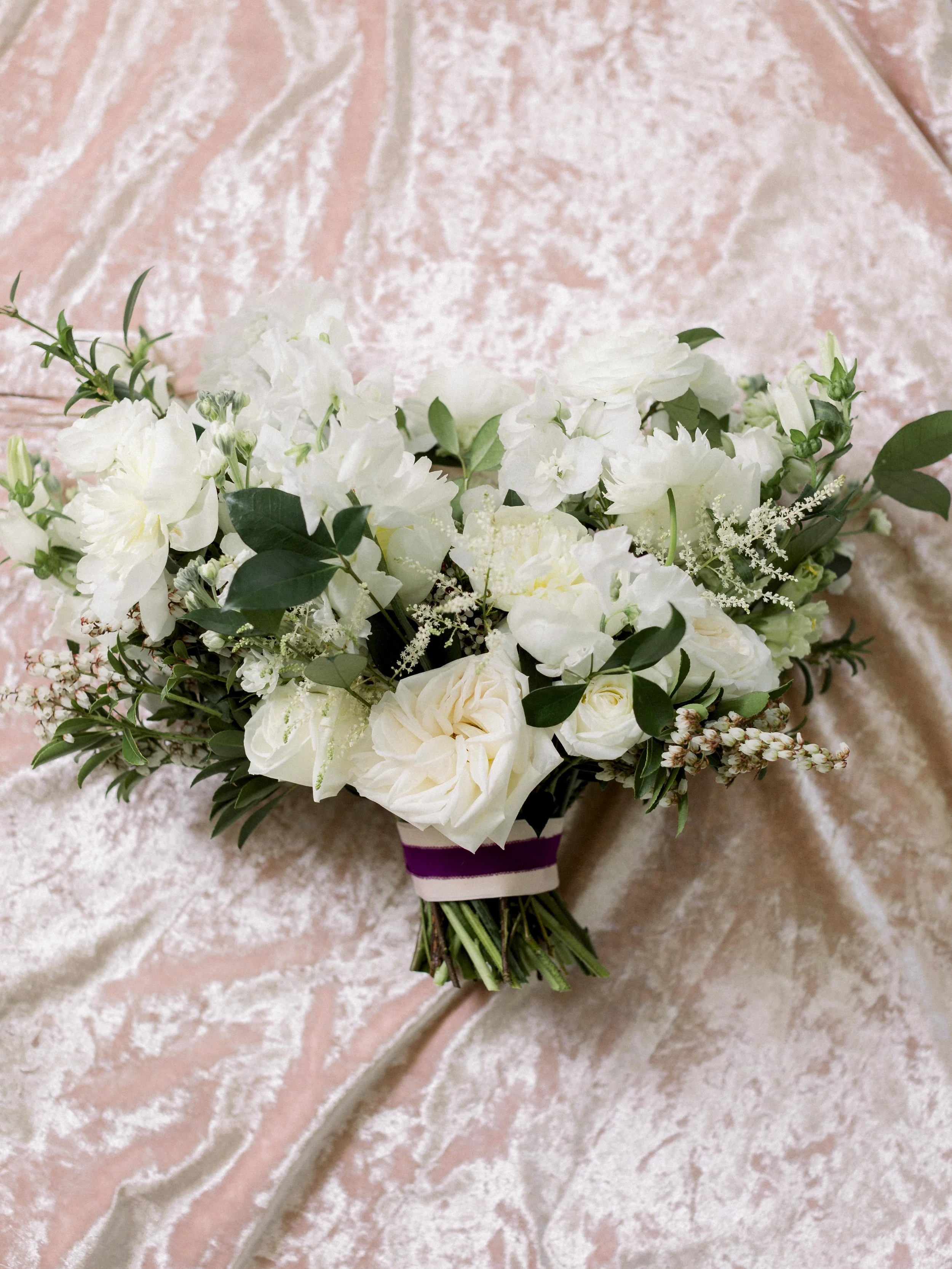 A bouquet of white flowers and greenery on a pink velvet surface.