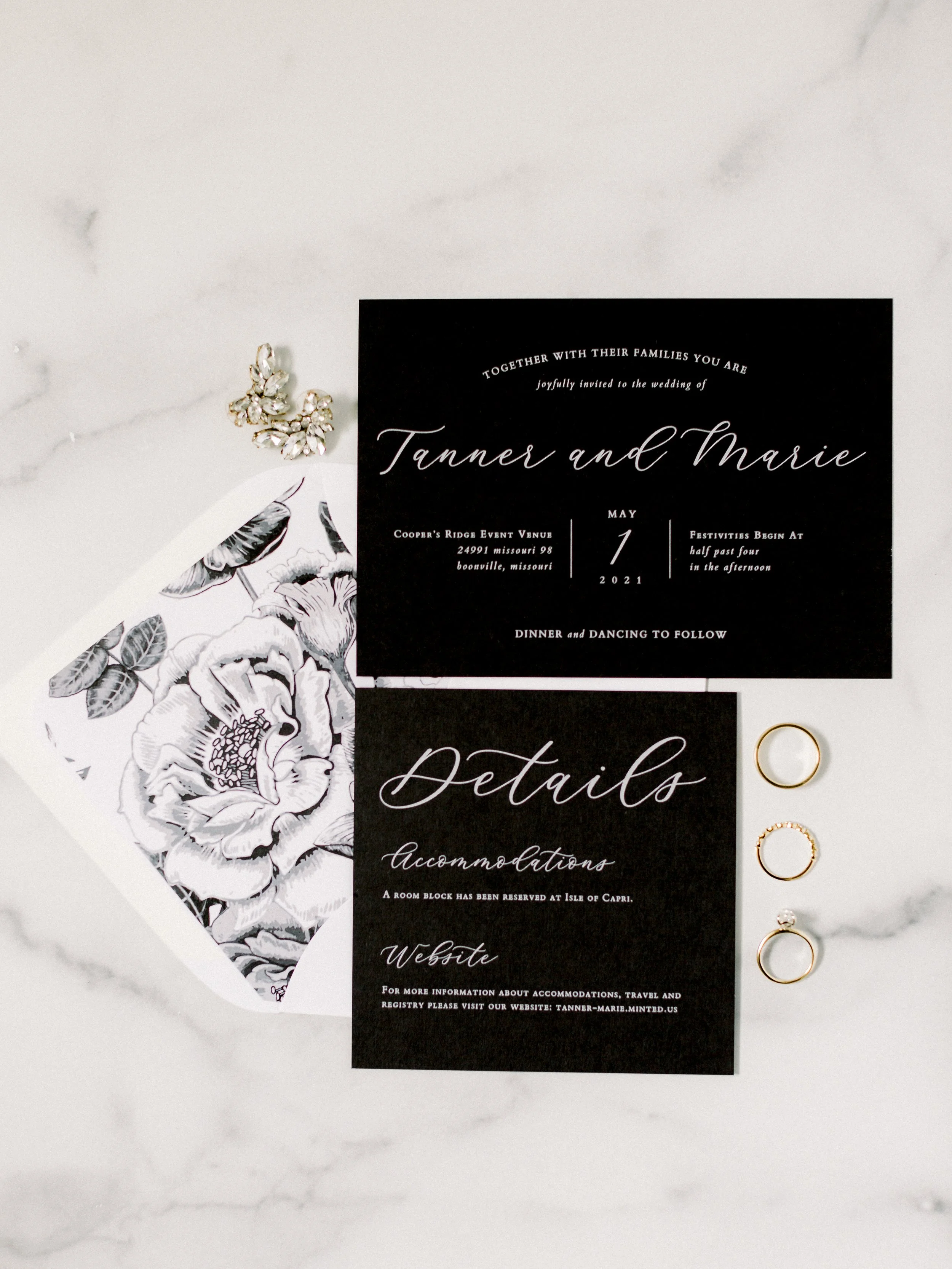 Wedding invitation card with black background and elegant white cursive text, alongside a floral illustration and four gold rings on the right side.