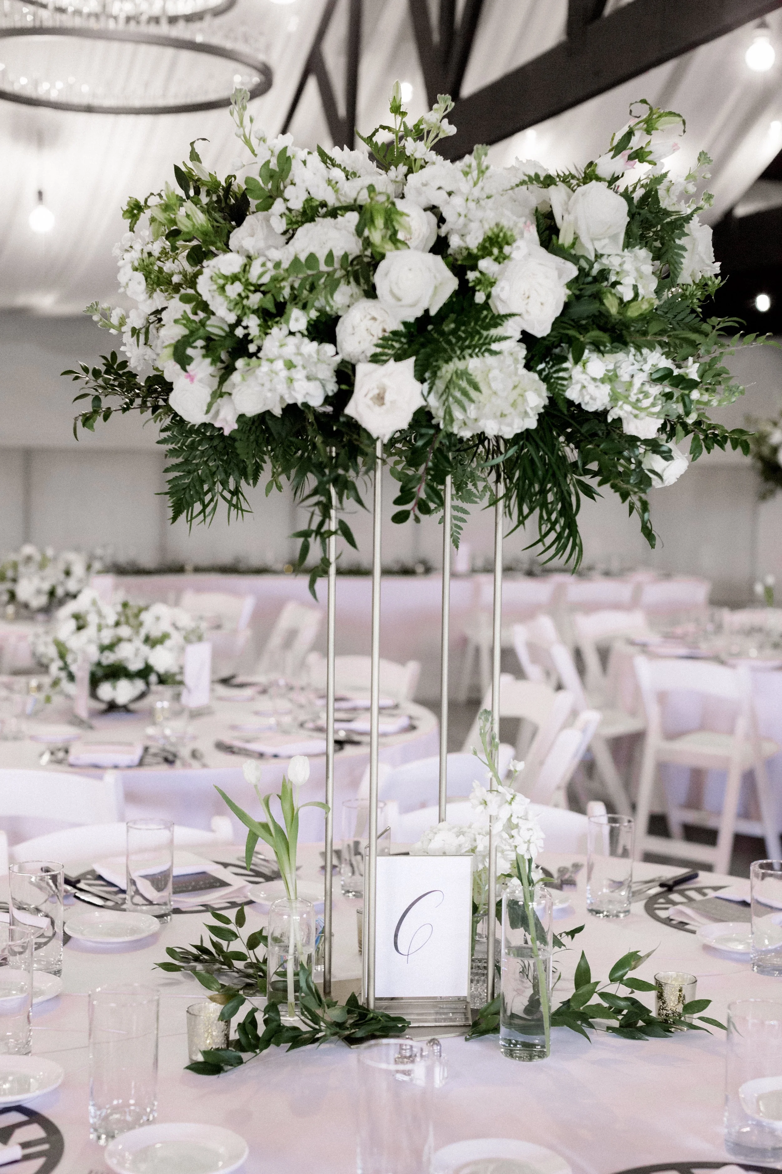 Table centerpiece with white flowers and greenery at a formal event in a decorated hall.