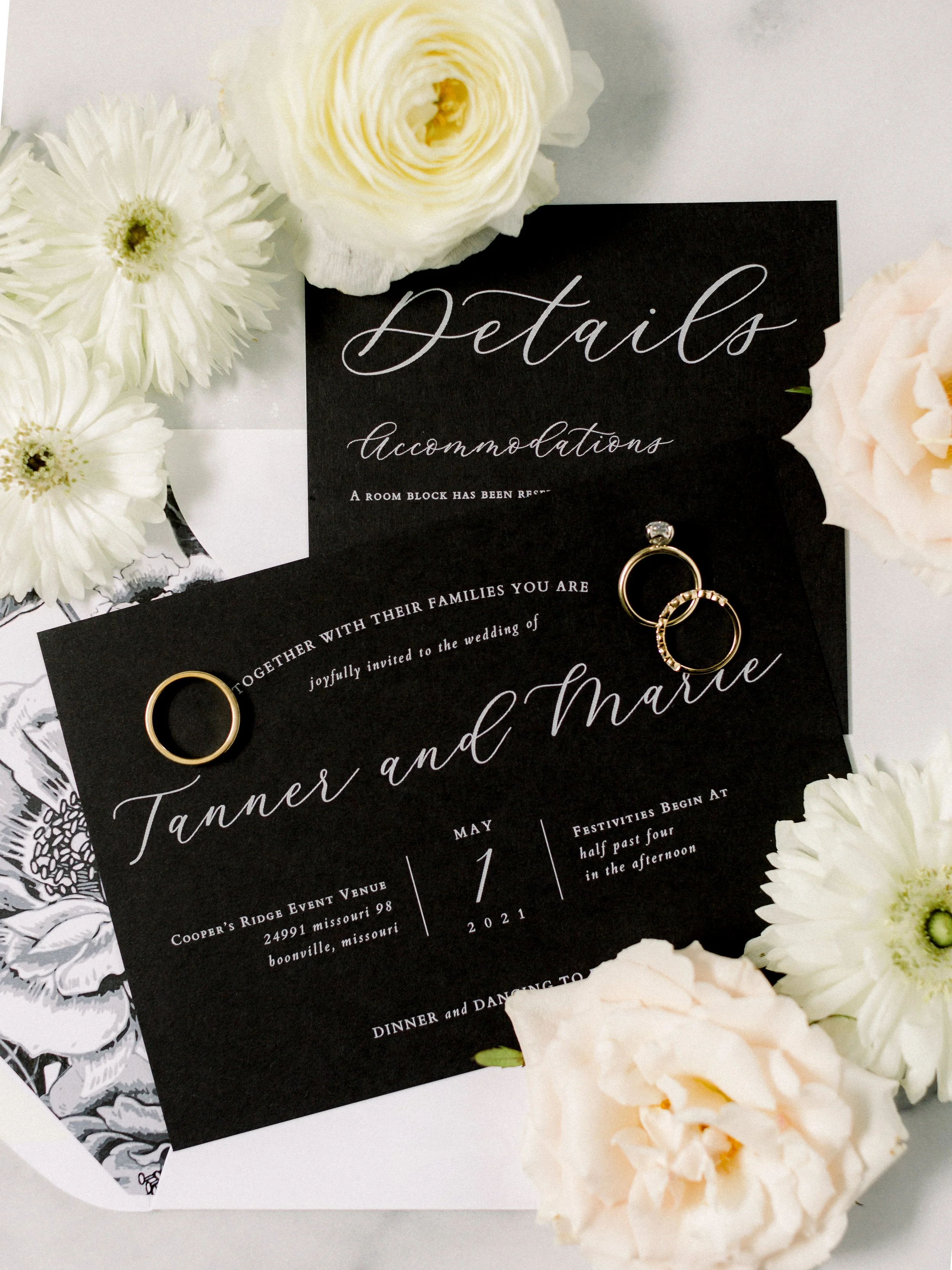 A wedding invitation card with elegant white flowers and gold rings on top.