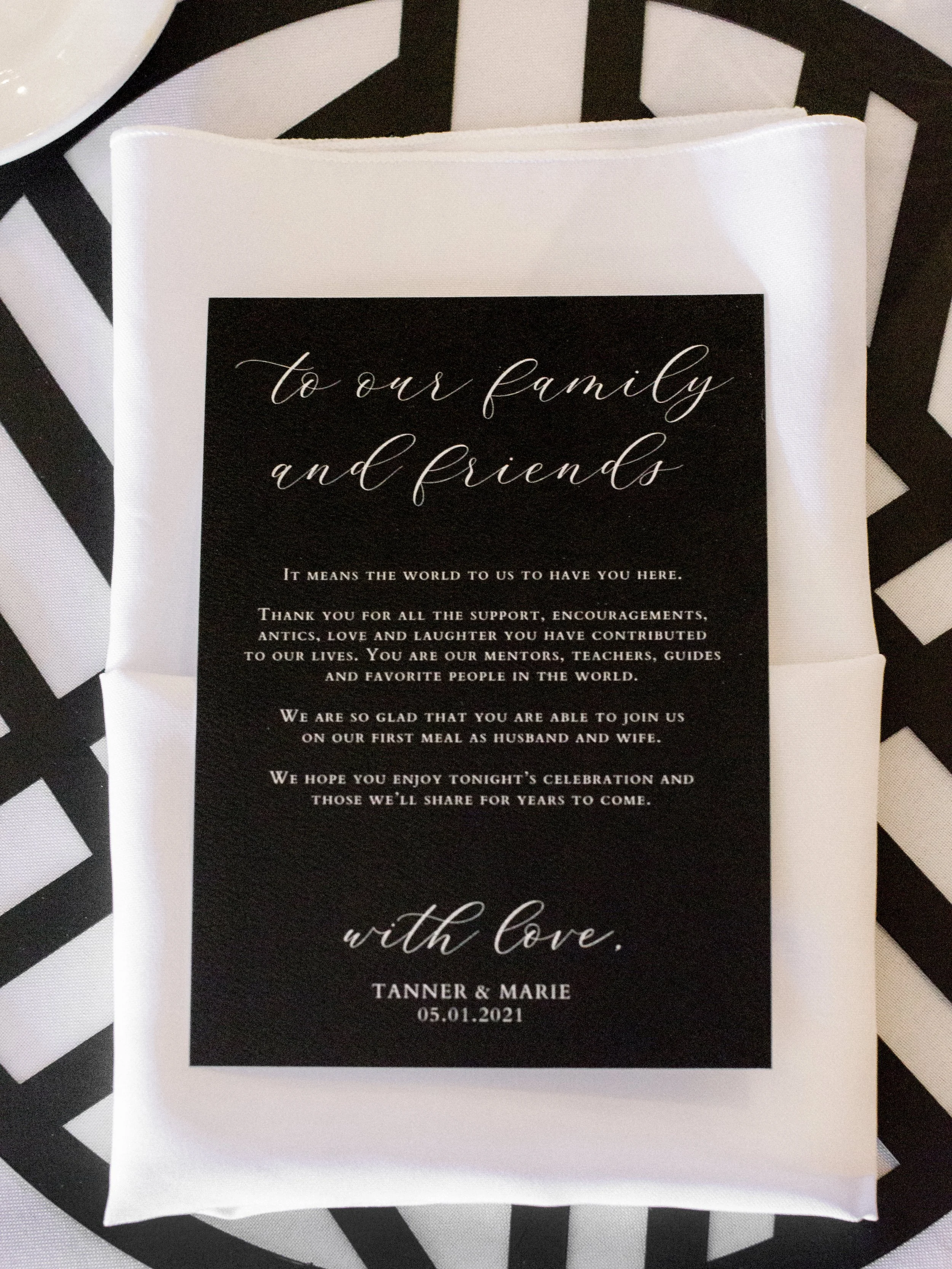 A black and white wedding program with elegant script text on a black background, placed on a black and white striped surface.