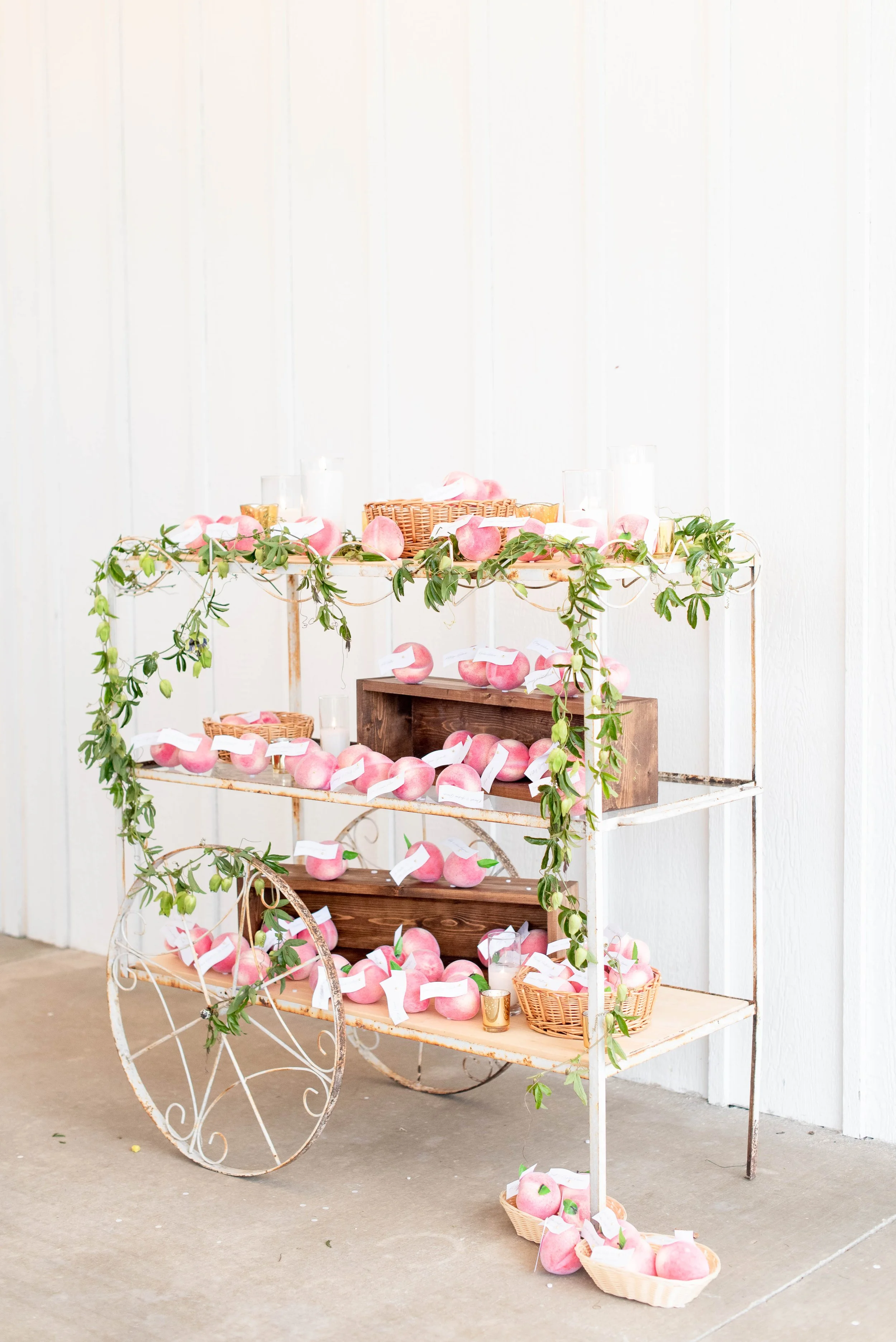 Display shelf with pink apples and green foliage, decorated for a wedding or event, against white wood-paneled wall.
