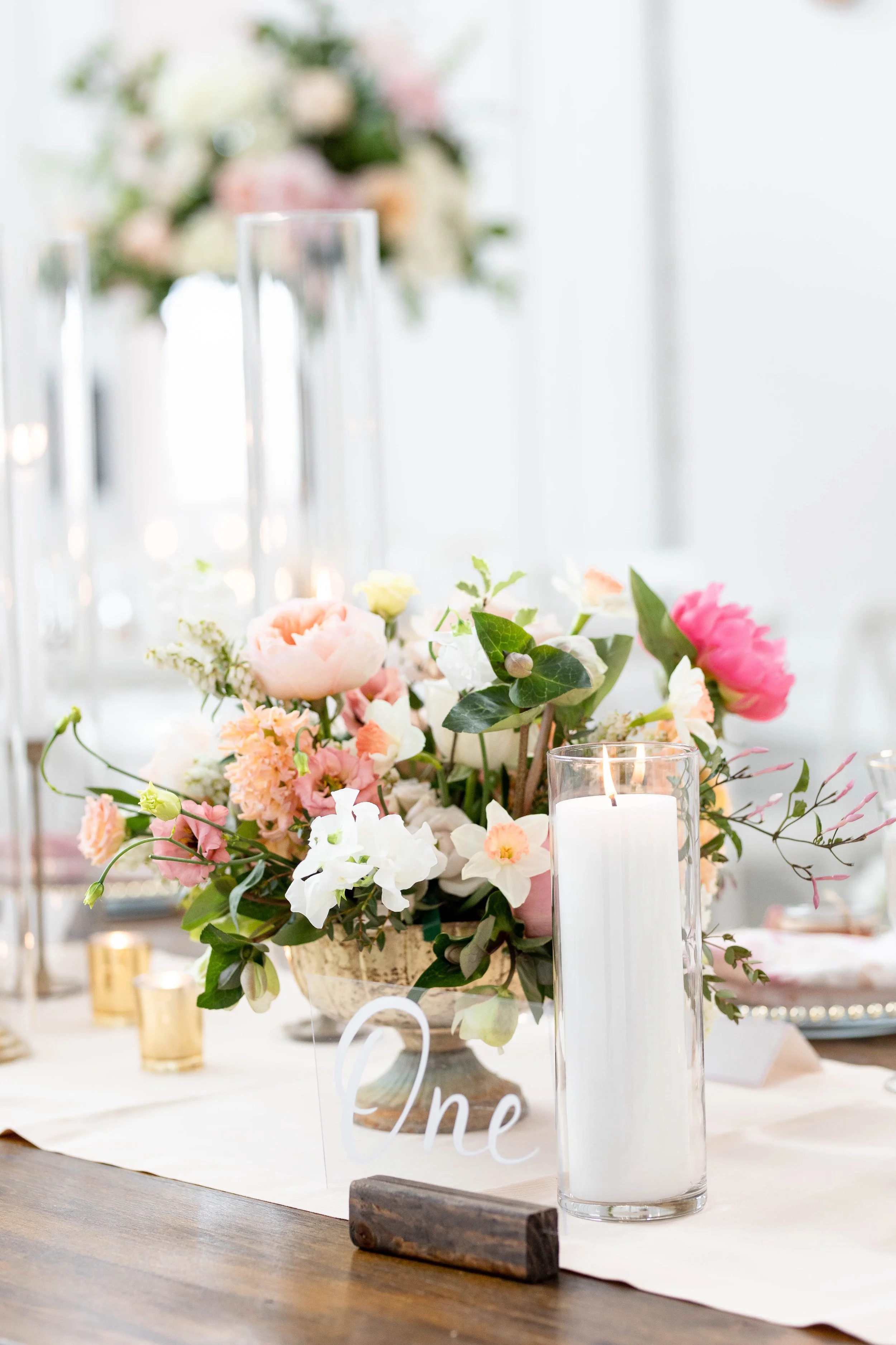 Elegant table centerpiece with pink, white, and peach flowers, candles, and greenery at a wedding reception or special event.