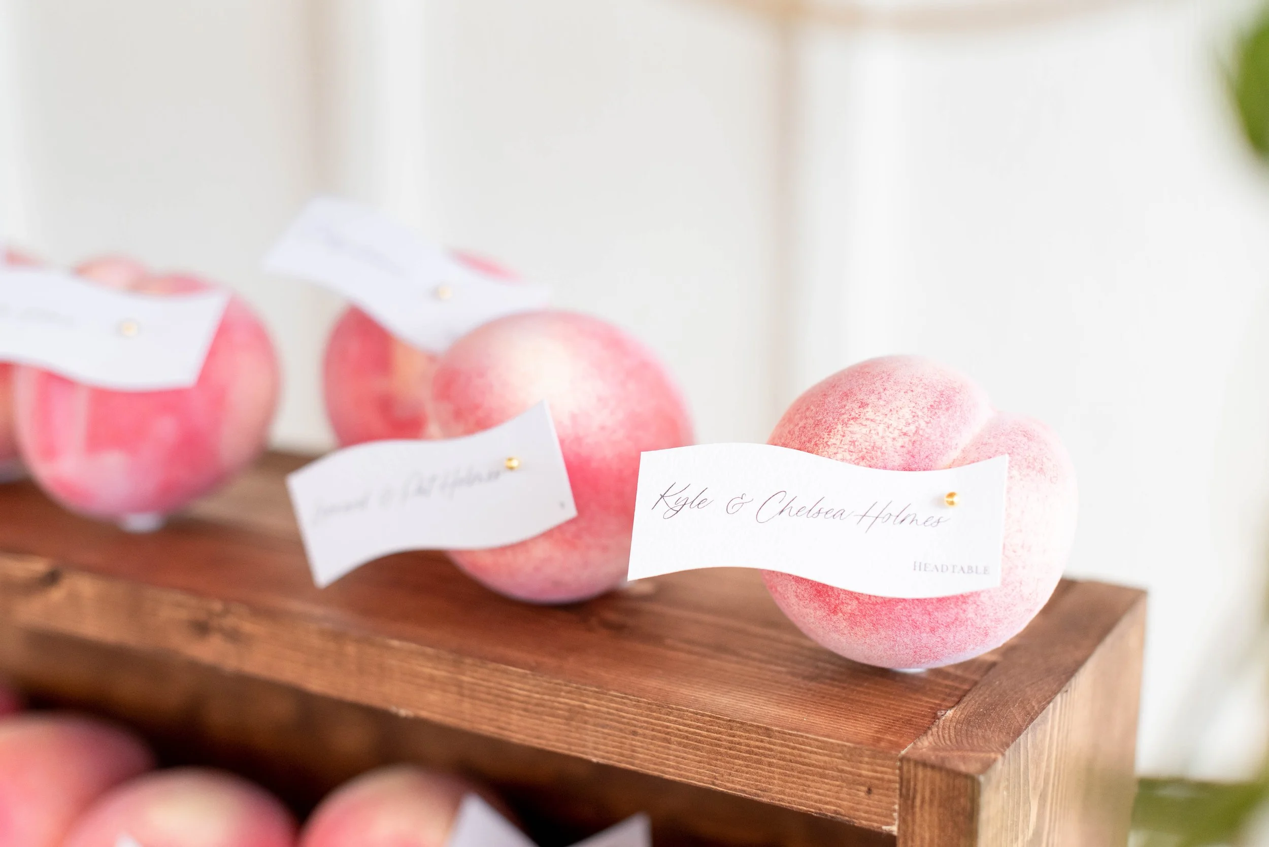 Several pink peaches with white tags on a wooden display in a market or store.
