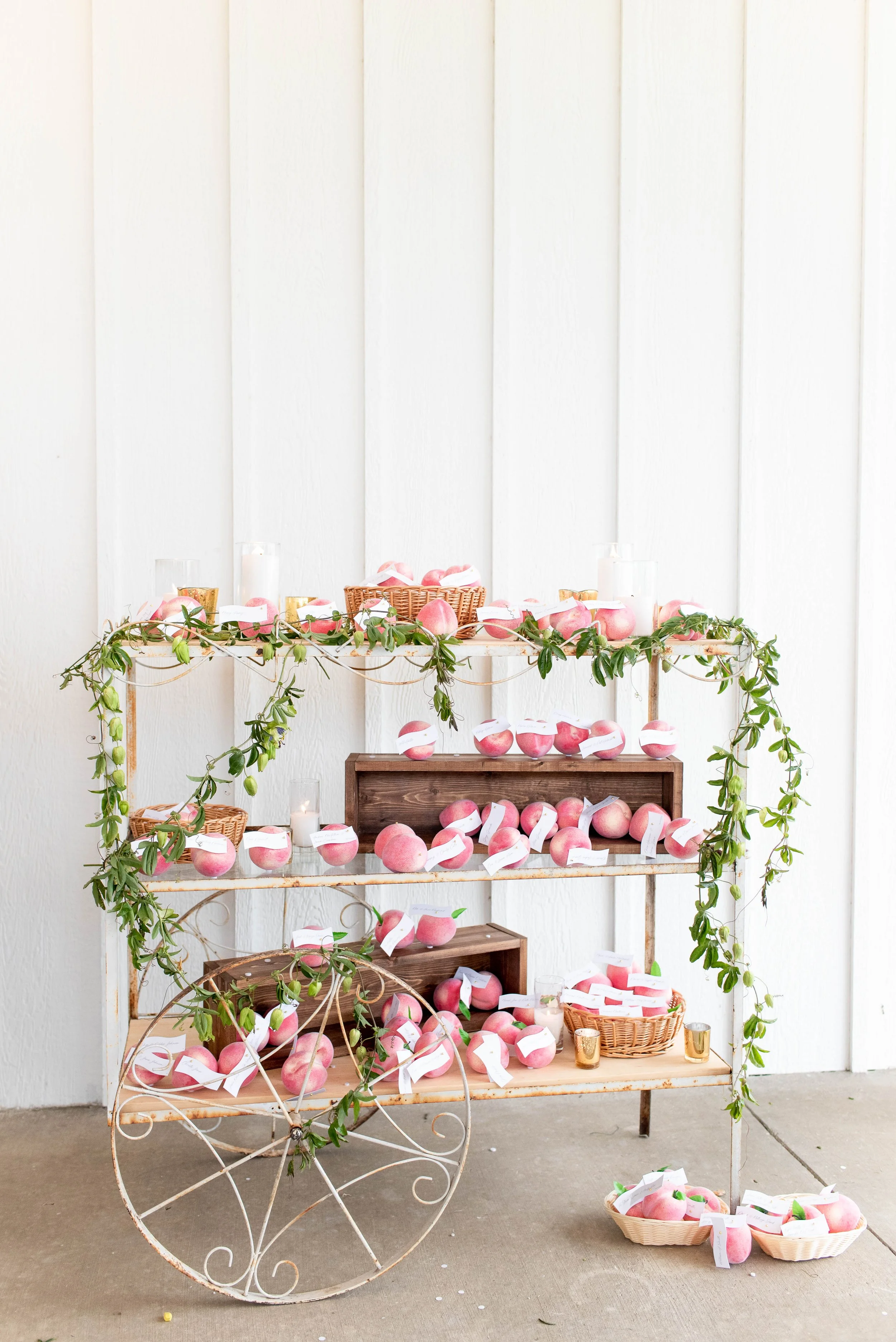 White wooden shelving unit decorated with pink apples and green vines, with baskets and candles, against a white wall.