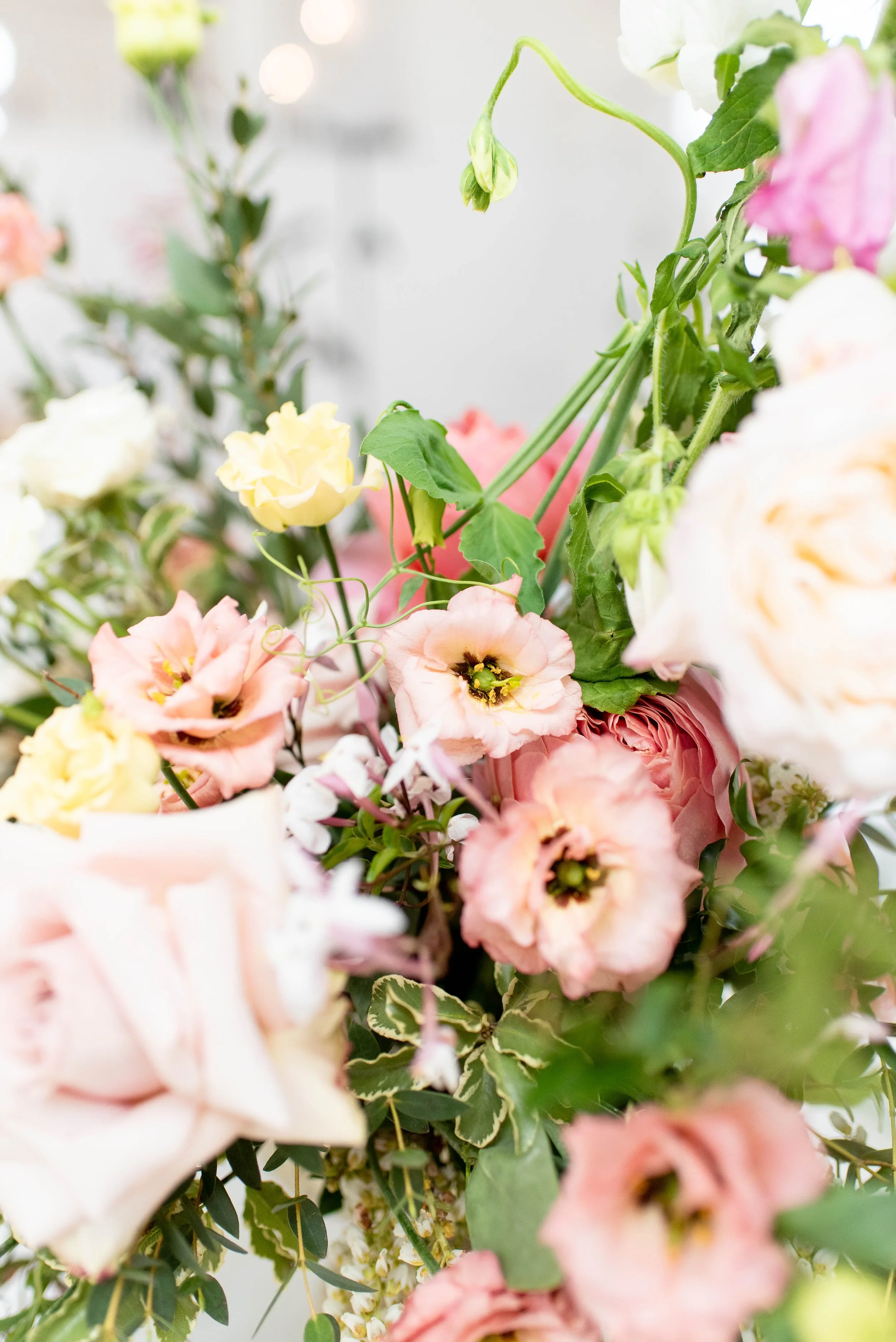 Close-up of an arrangement of various pastel-colored flowers including pink, peach, white, and yellow, with green leaves and stems.