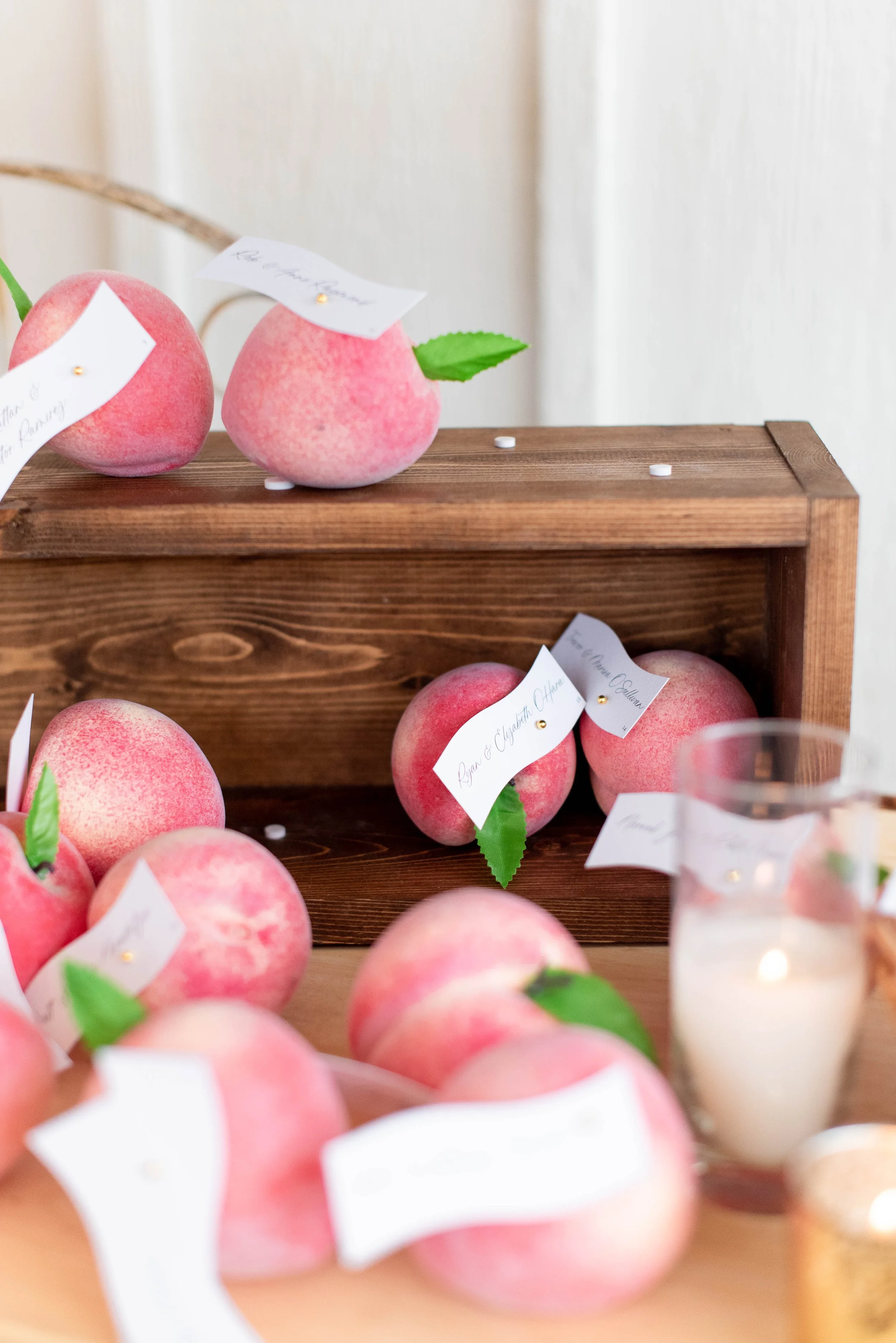 Display of pink peaches with green leaves on a wooden shelf, with small white notes attached.