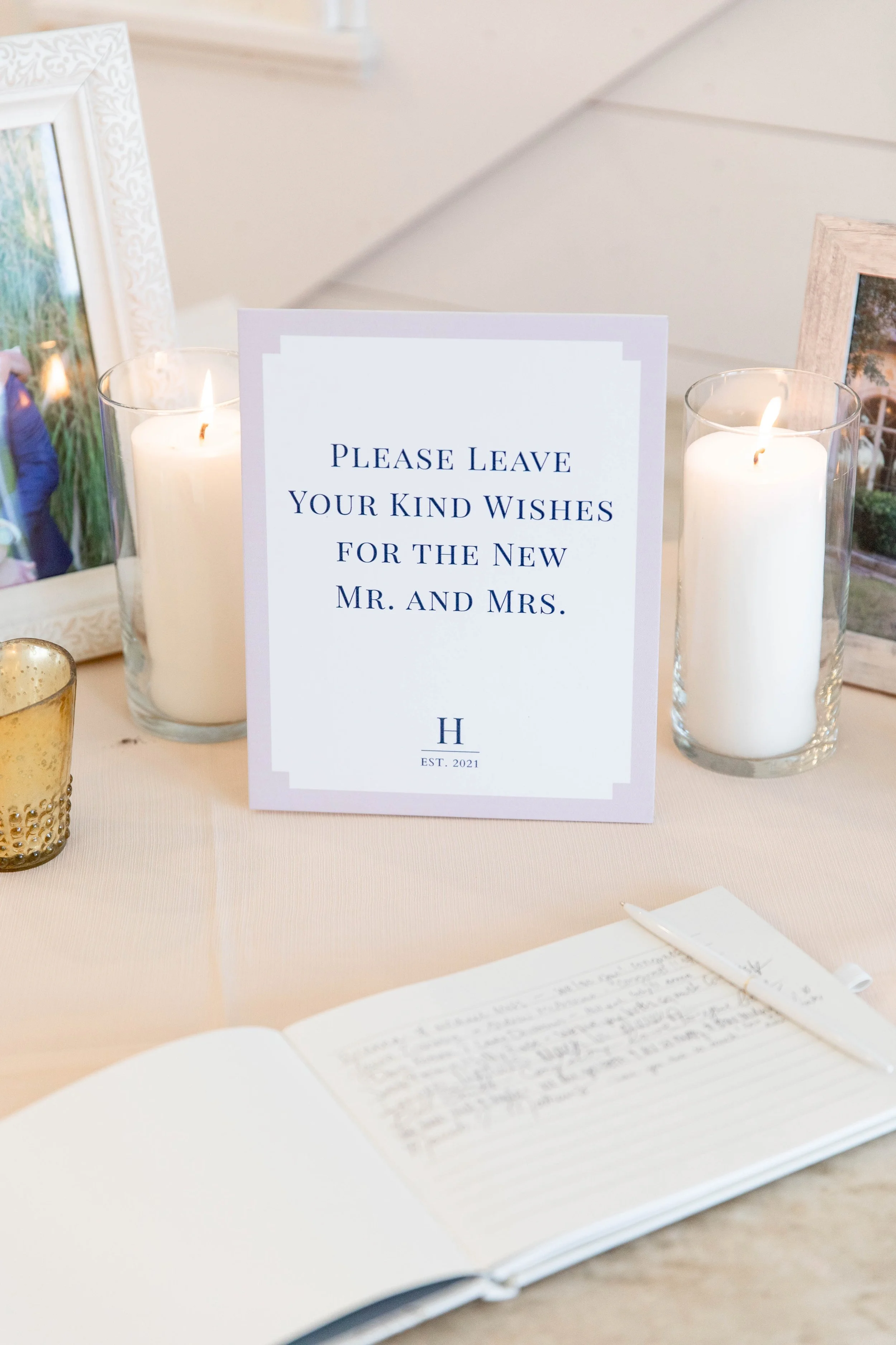 A wedding guest book with an open page, surrounded by candles and framed photographs, with a sign that reads, 'Please leave your kind wishes for the new Mr. and Mrs.'