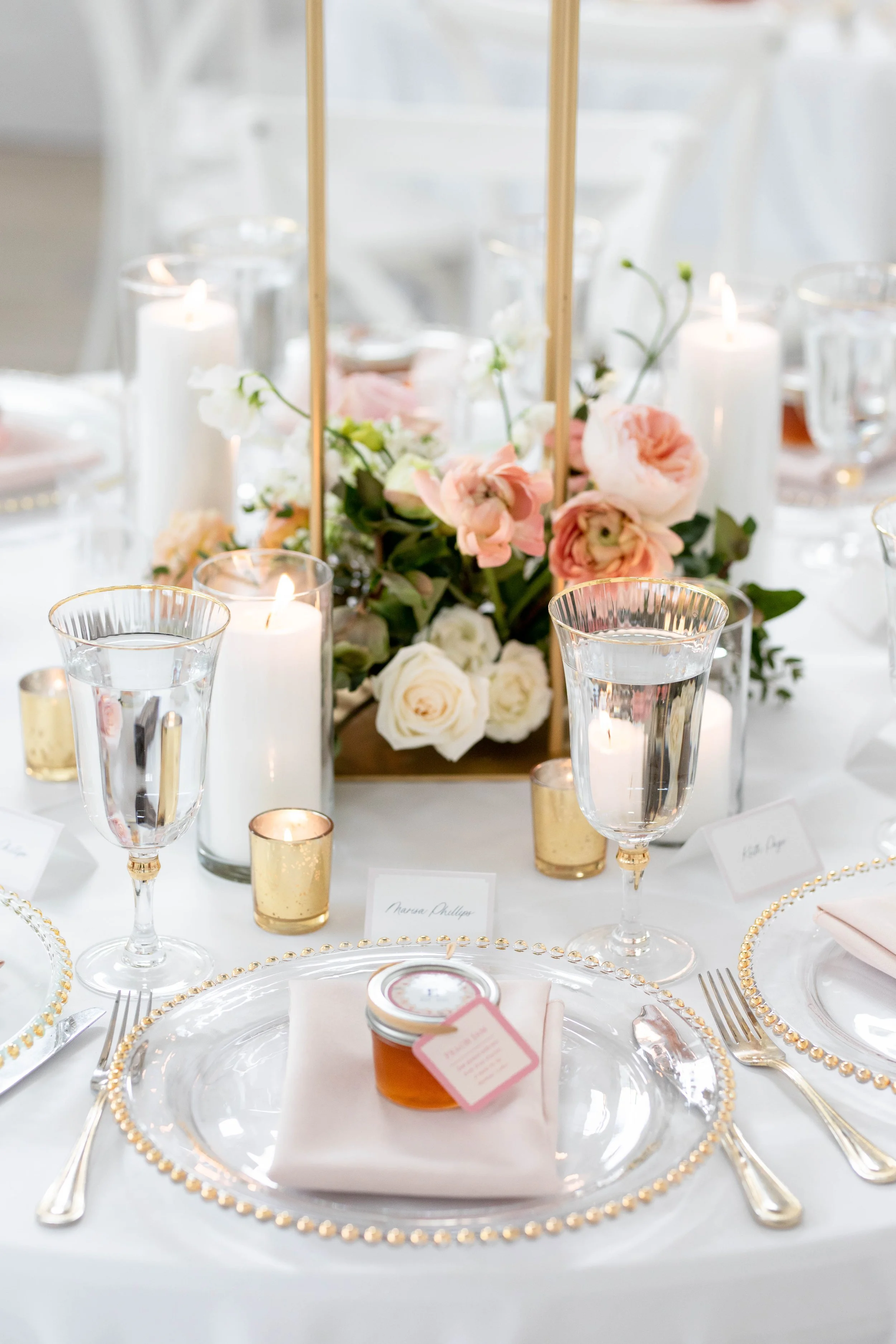 Decorative table setting with floral centerpiece, candles, gold-rimmed glassware, and plates at a formal event or wedding reception.