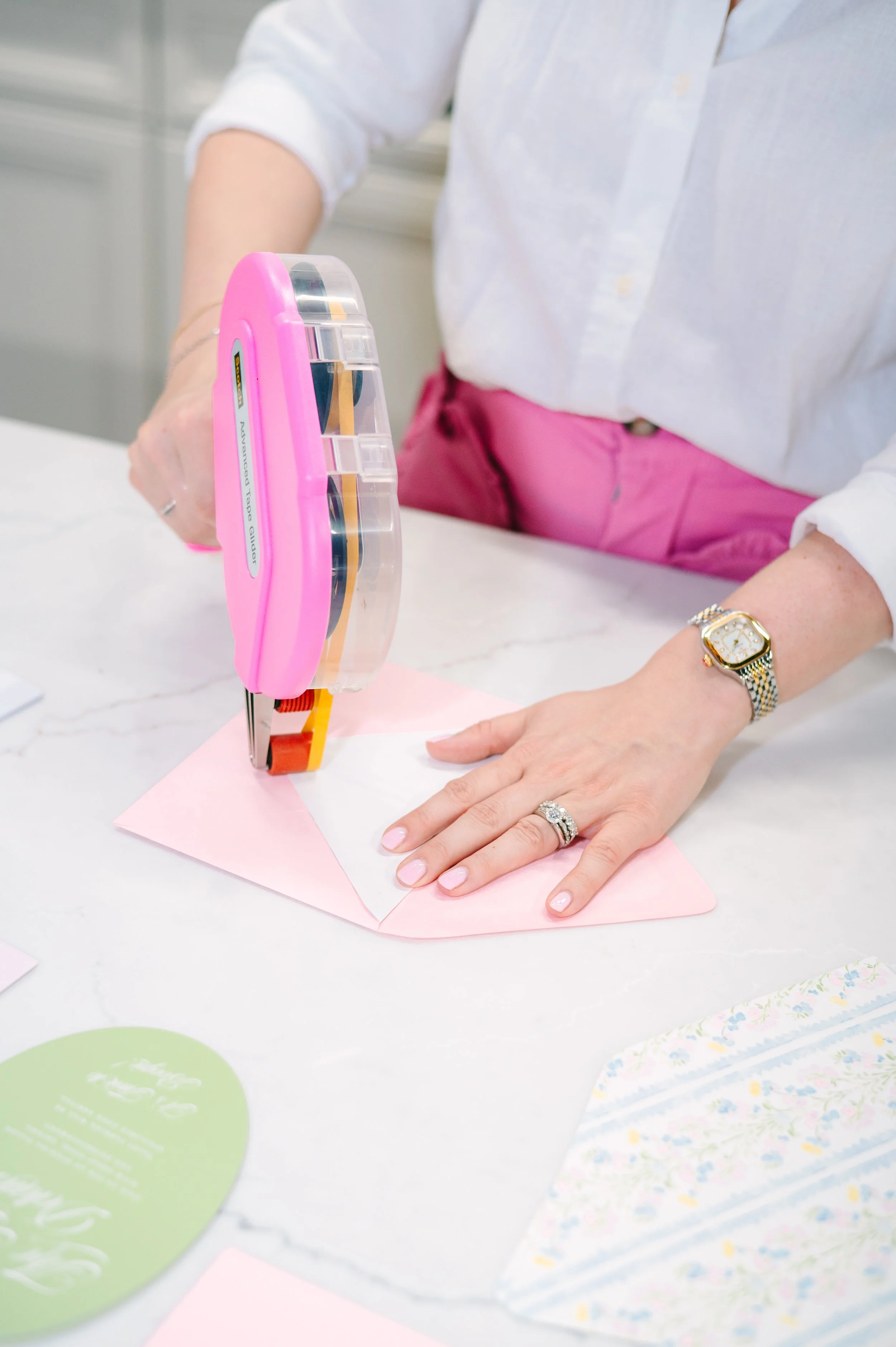 Person using tape dispenser to attach a piece of pink and white paper to a surface.